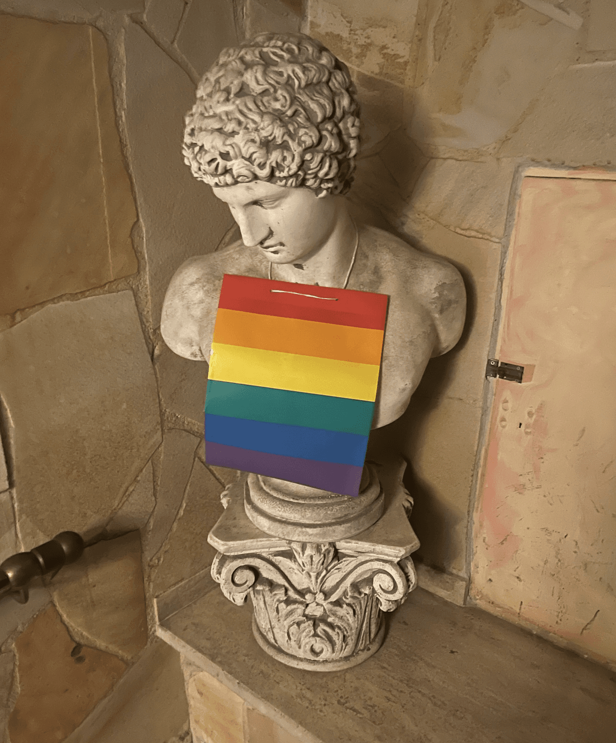 A statue with a rainbow flag draped over him. 