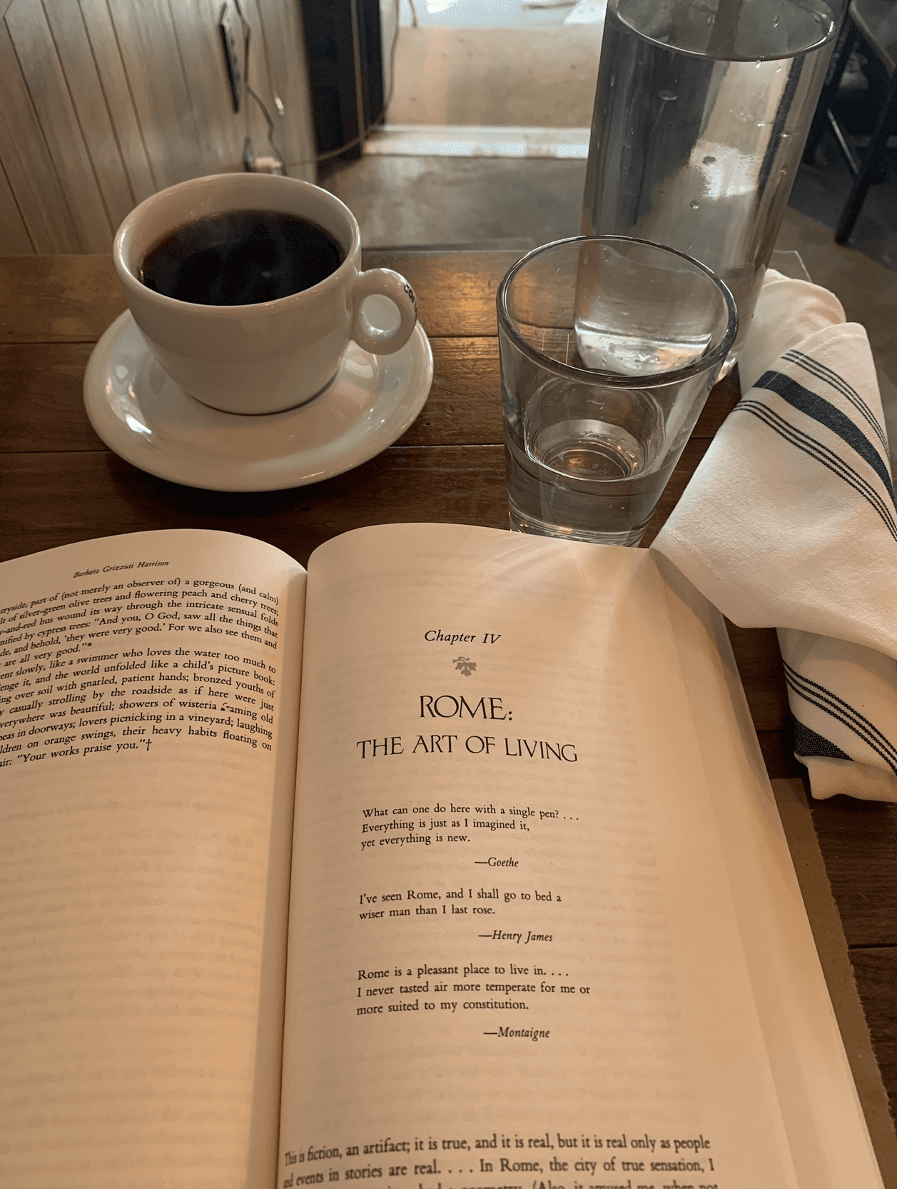 An image of a book on a table with cup of coffee and water. 