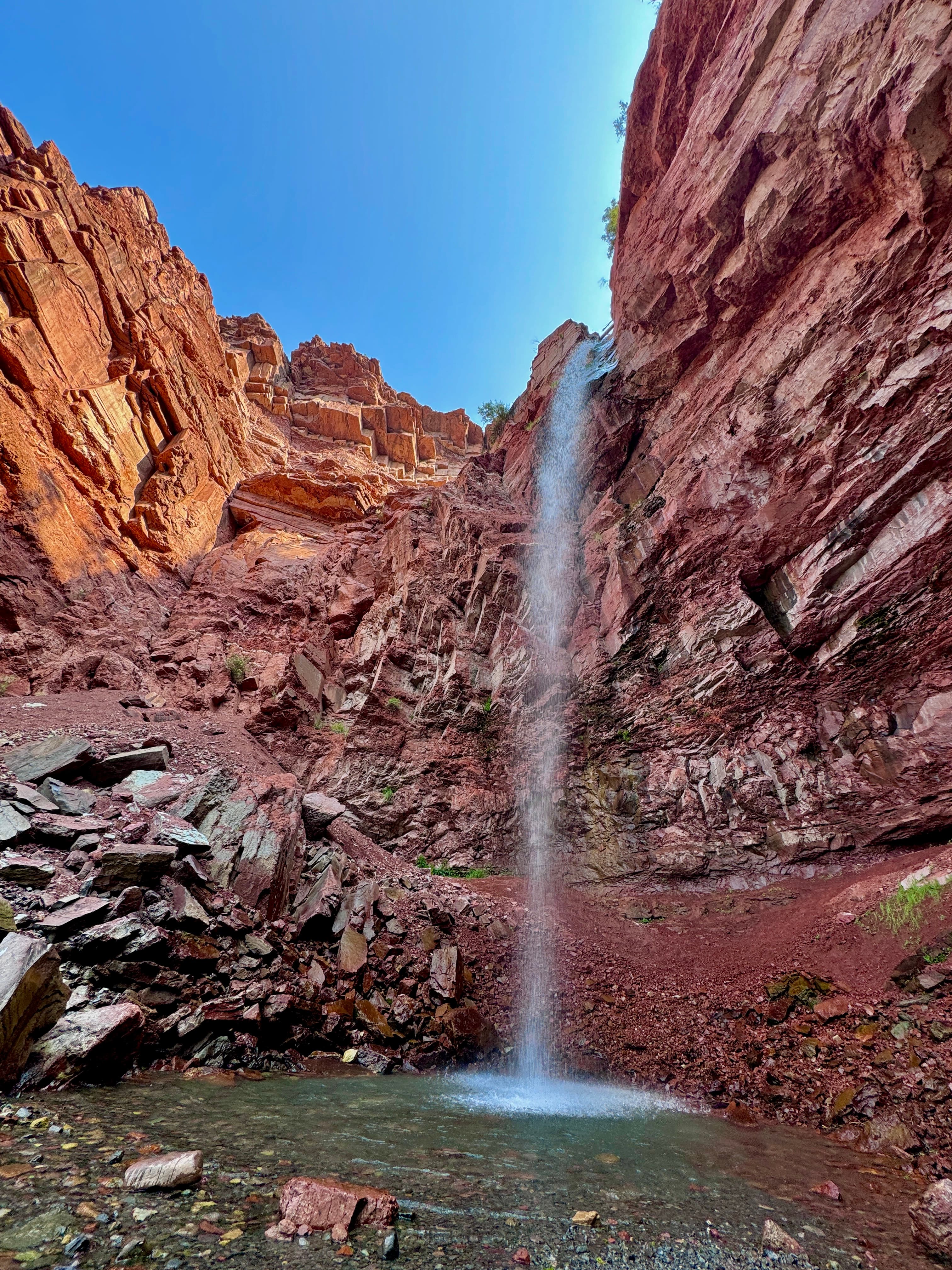 View of a small waterfall falling from red rock cliffs on a sunny day