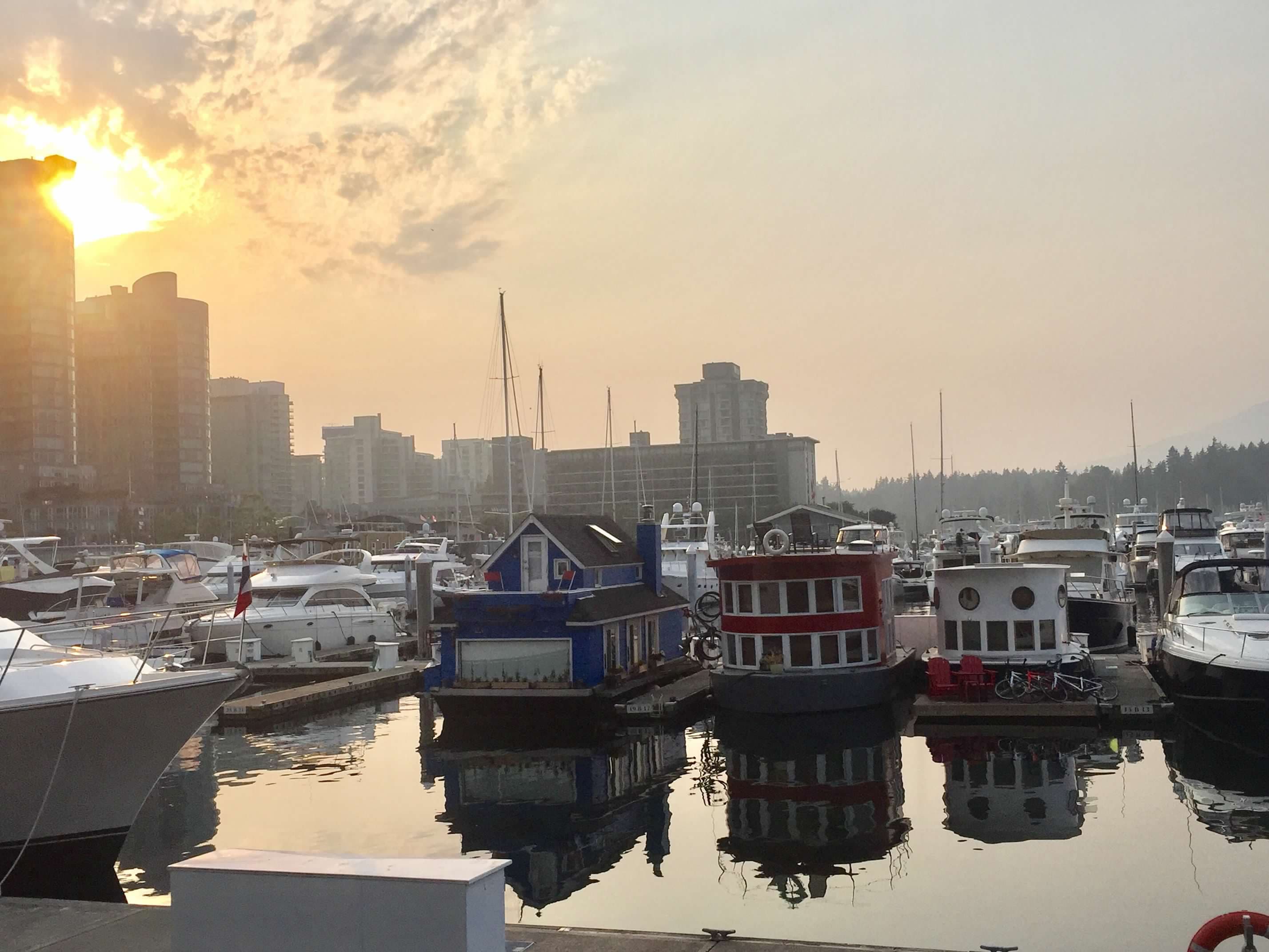 Boats fill a harbor as the sun sets and gives off an orange hue on a clear day. 