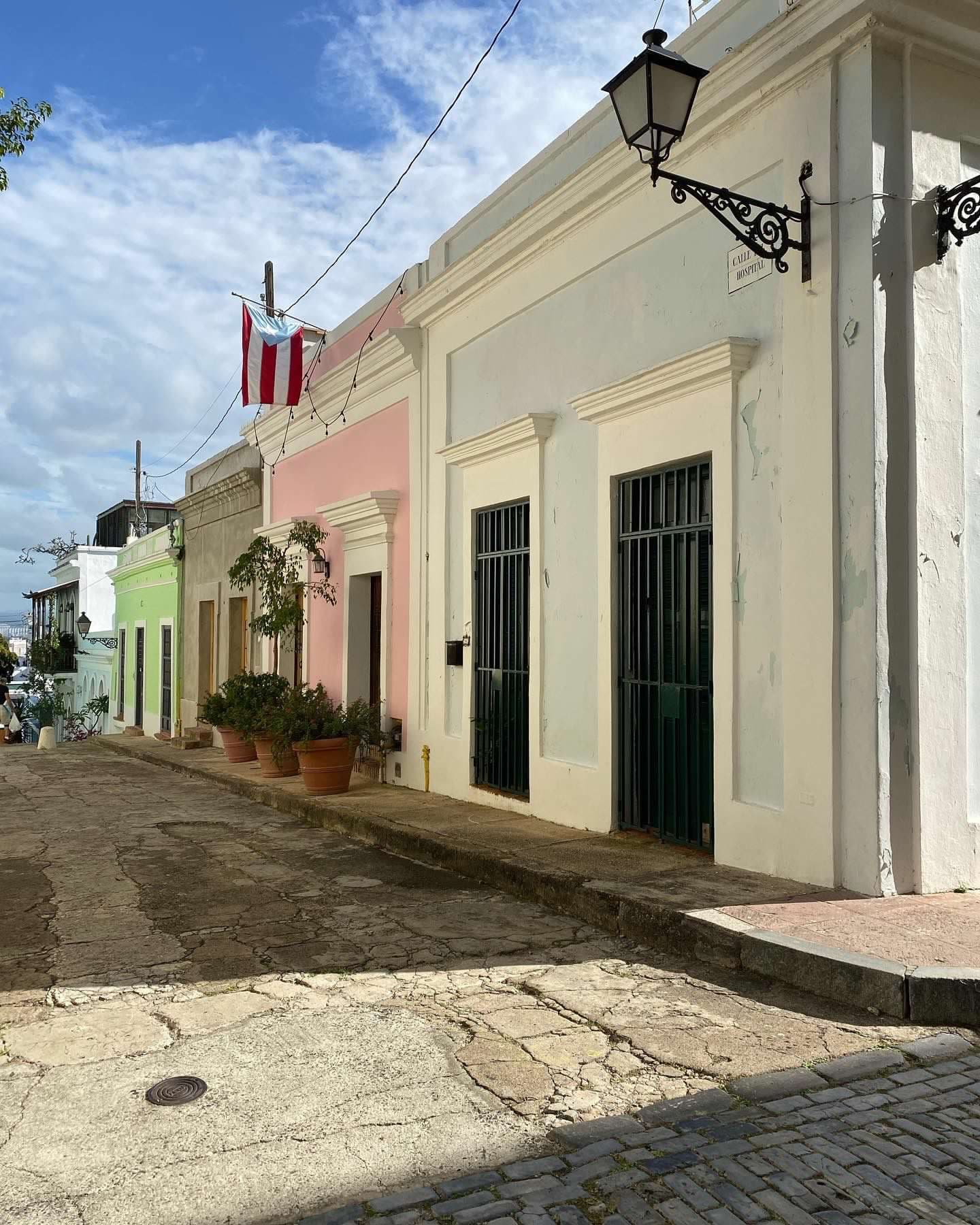 Brightly colored shops line a quaint street on a sunny day dotted with clouds. 