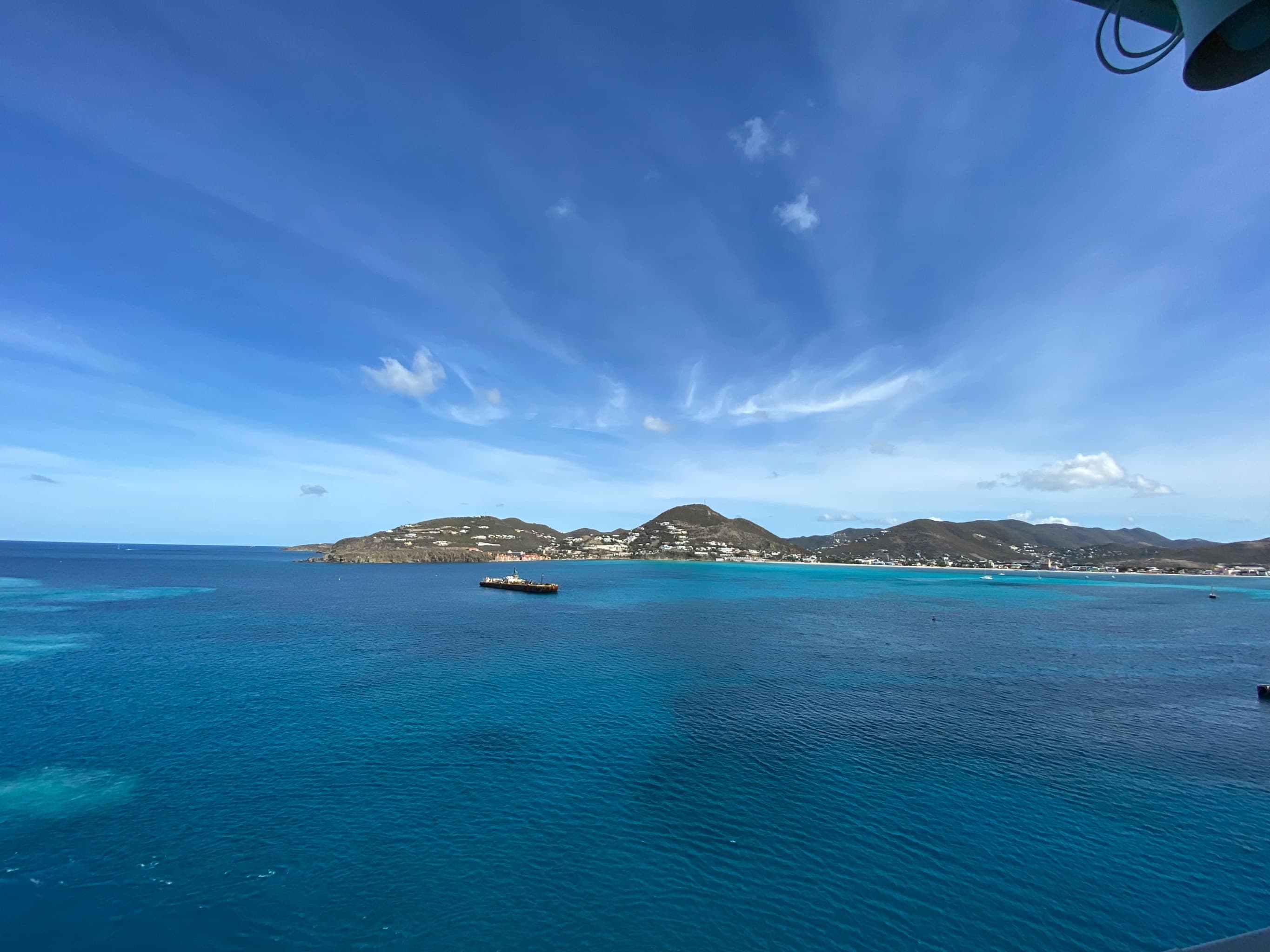 Crystal-clear waters sweep across the horizon with a hilly island in the distance on a clear day. 