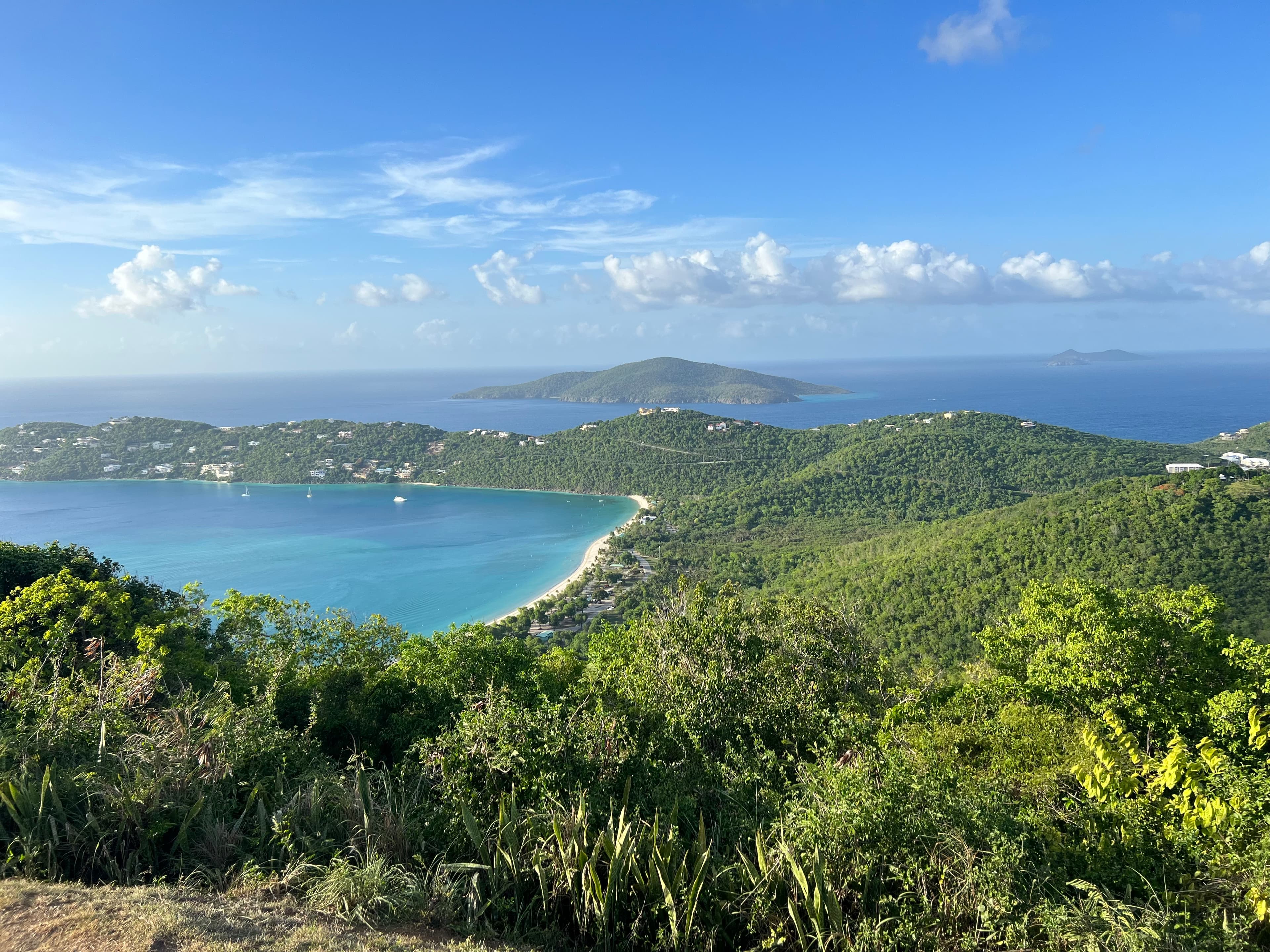 Beautiful aerial view of lush green hills and a wide bay with white sand beach under sunny skies