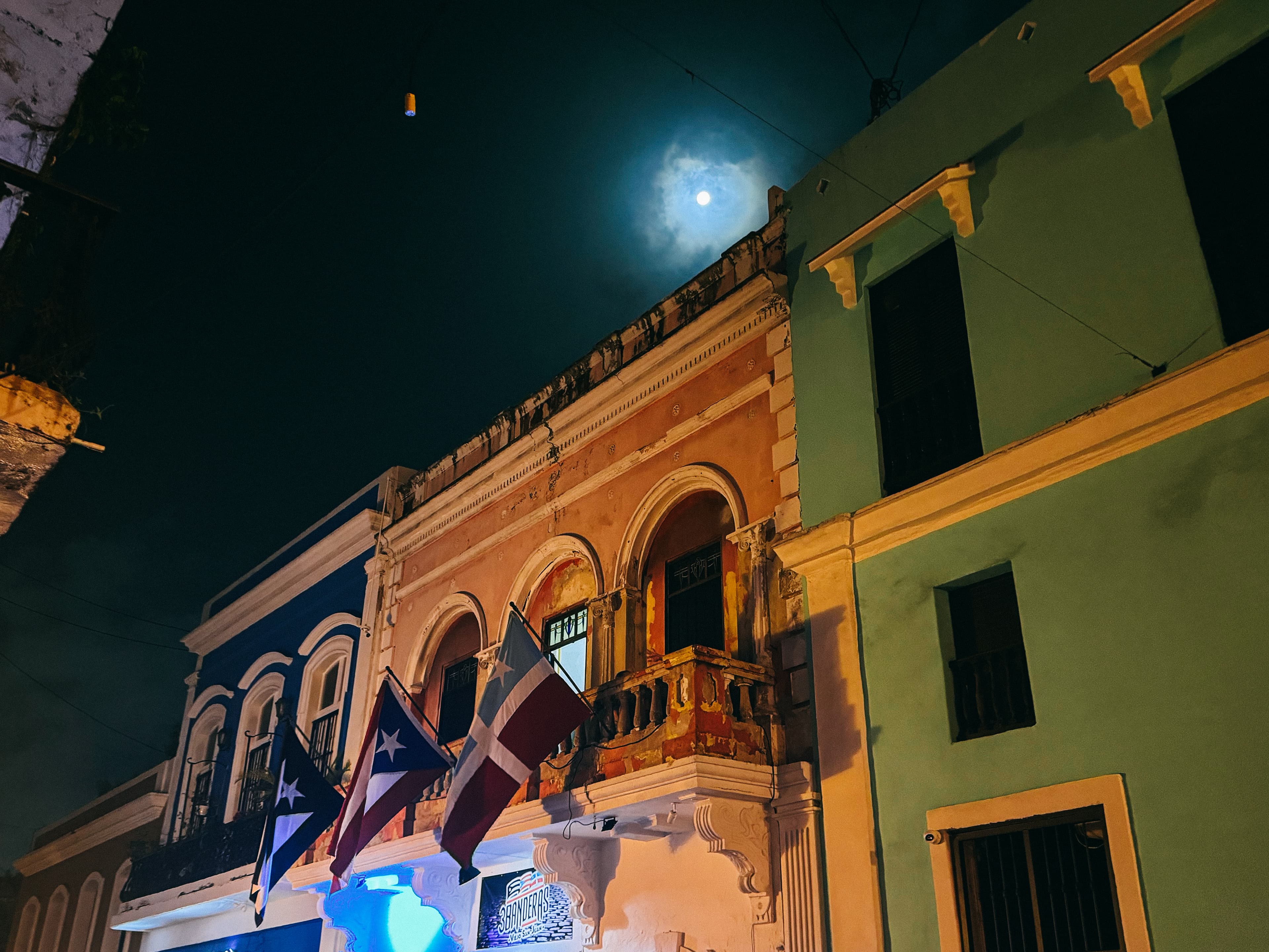 Low-angled view of old buildings with three flags flying against a night sky.