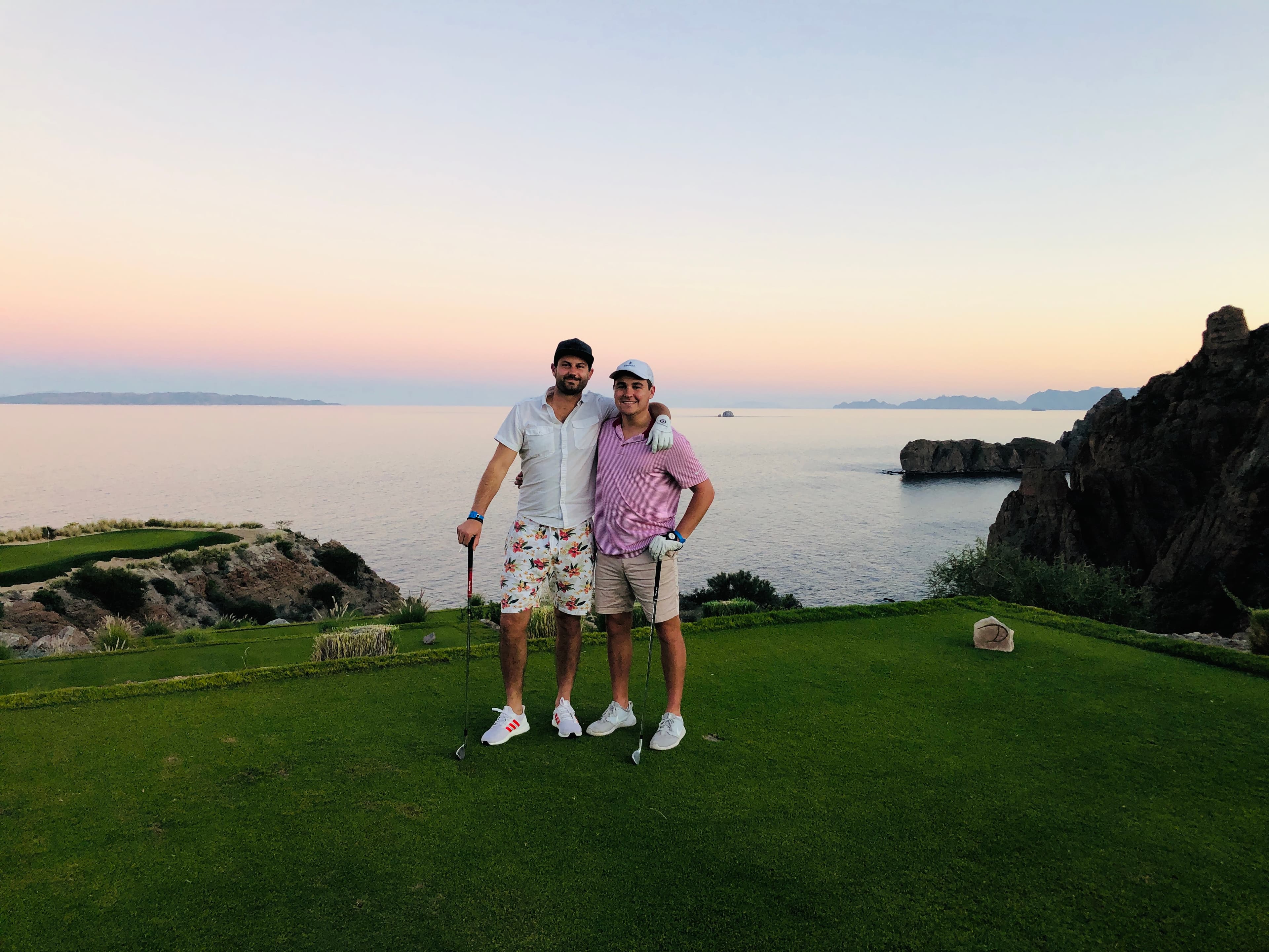 Advisor and a friend playing golf at a hole overlooking a beautiful coastal area at sunset