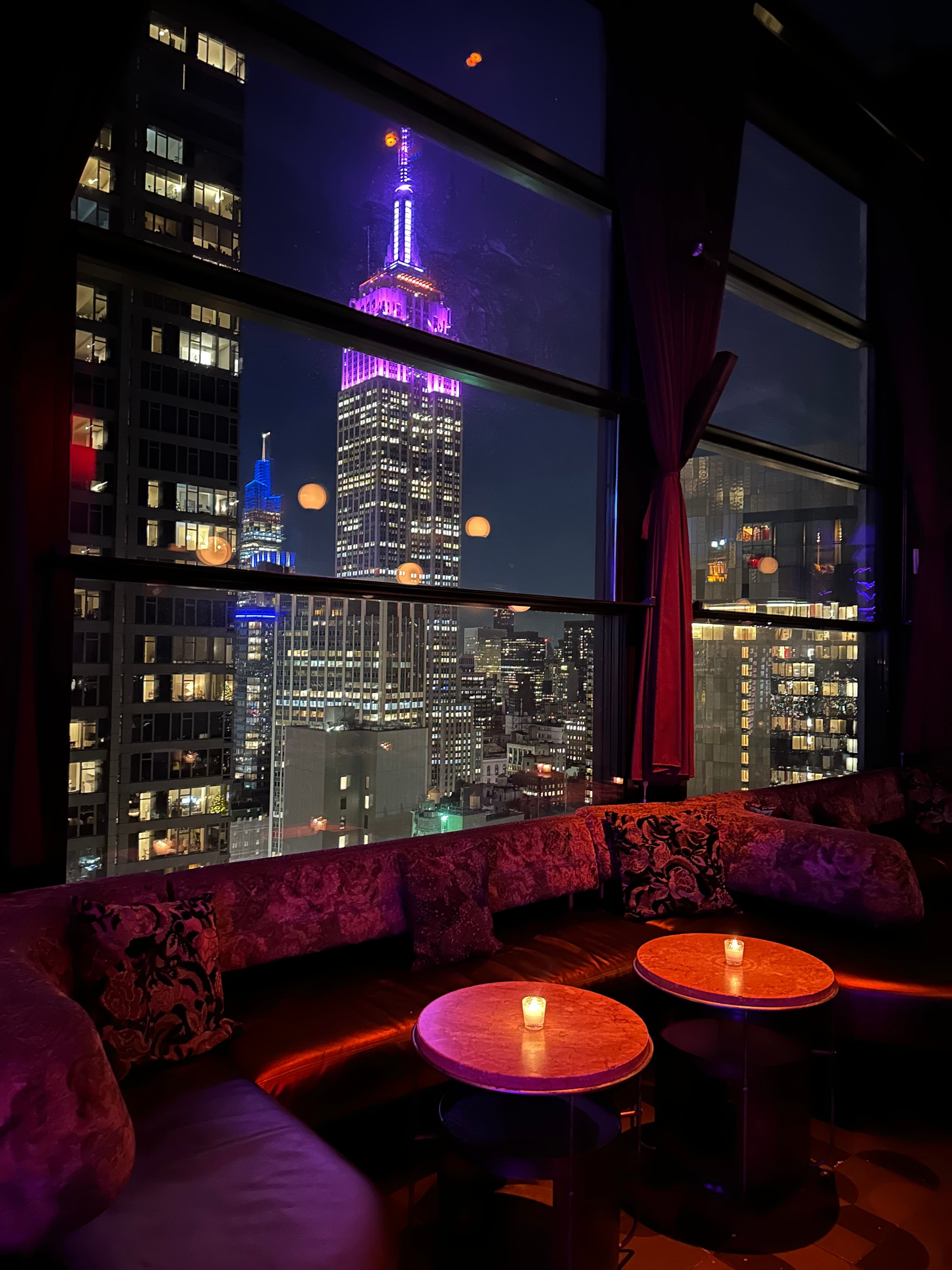 View of the Empire State Building lit up in purple light as seen through a window at night