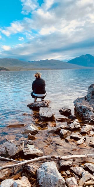 Advisor perched on a rock at the edge of a large lake, mountains surrounding it in the distance 