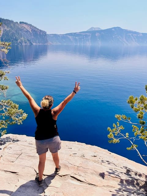 Advisor standing on a cliff with arms raised looking out over a beautiful lake surrounded by cliffs