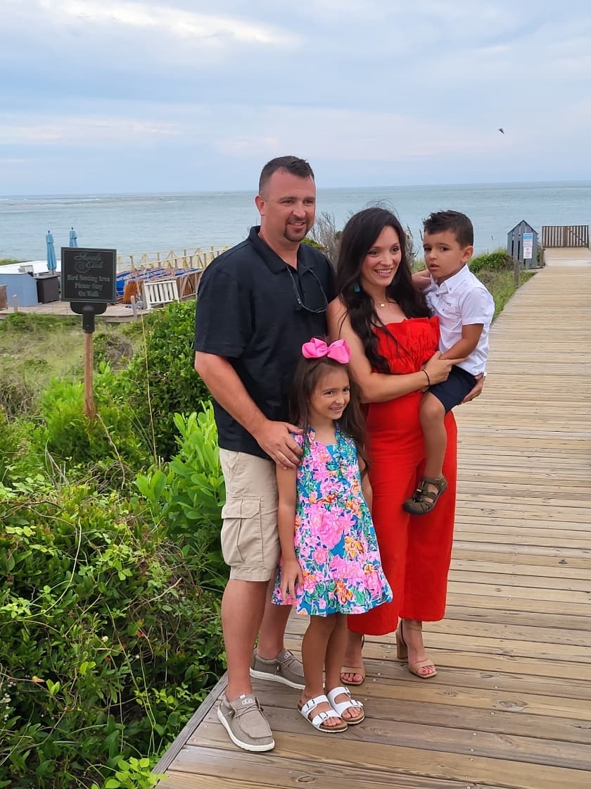 Advisor and her family posing on a wooden boardwalk by the sea on a cloudy afternoon