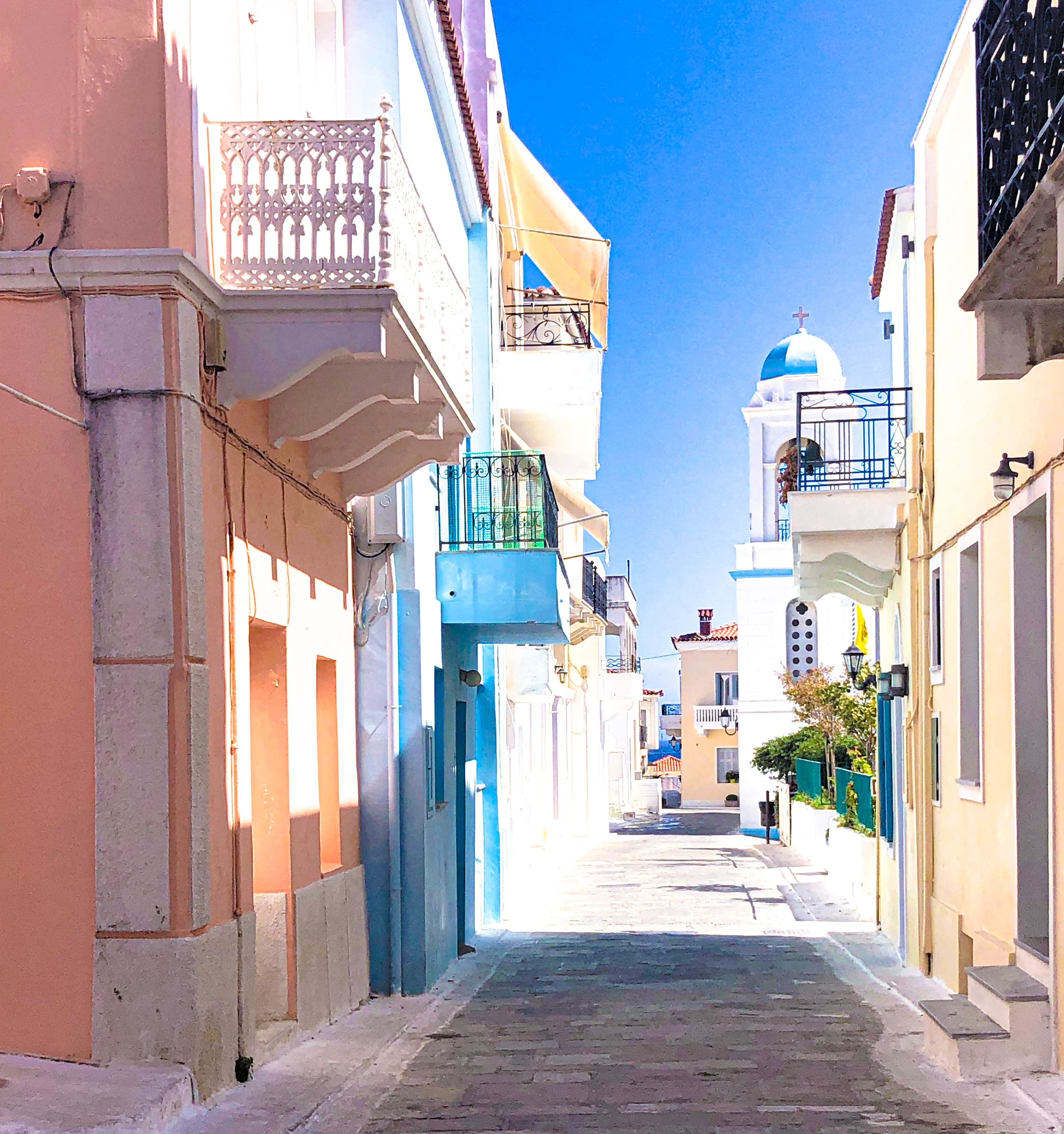 View of an empty stone street lined with small, colorful buildings on a sunny day