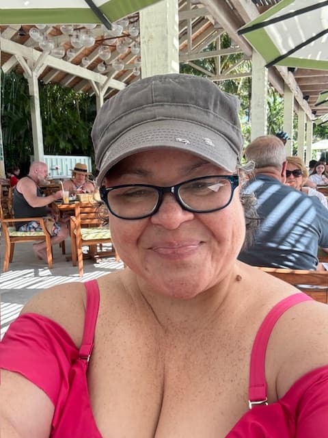 Advisor in a pink shirt and cap taking a selfie outdoors on a restaurant patio during the day