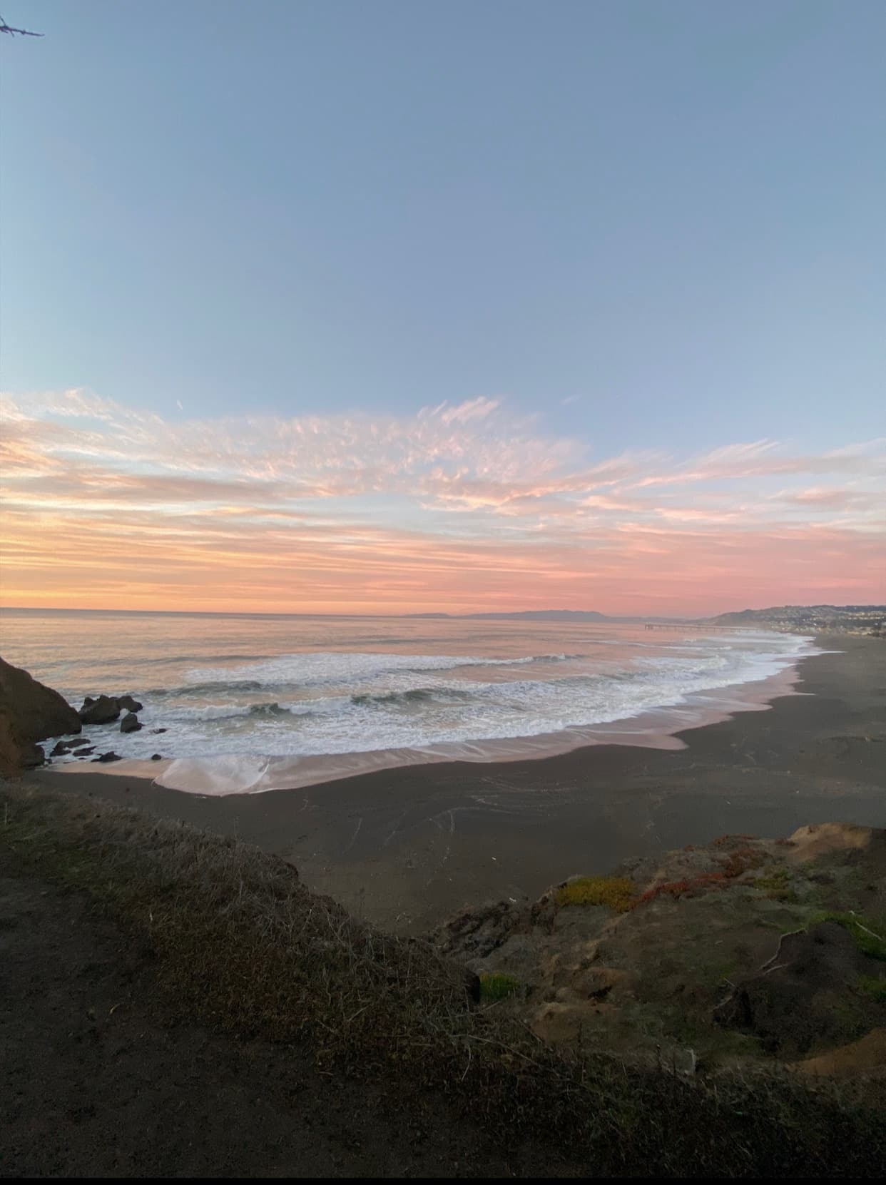 View of an empty beach with calm ocean waters and a light pink sky
