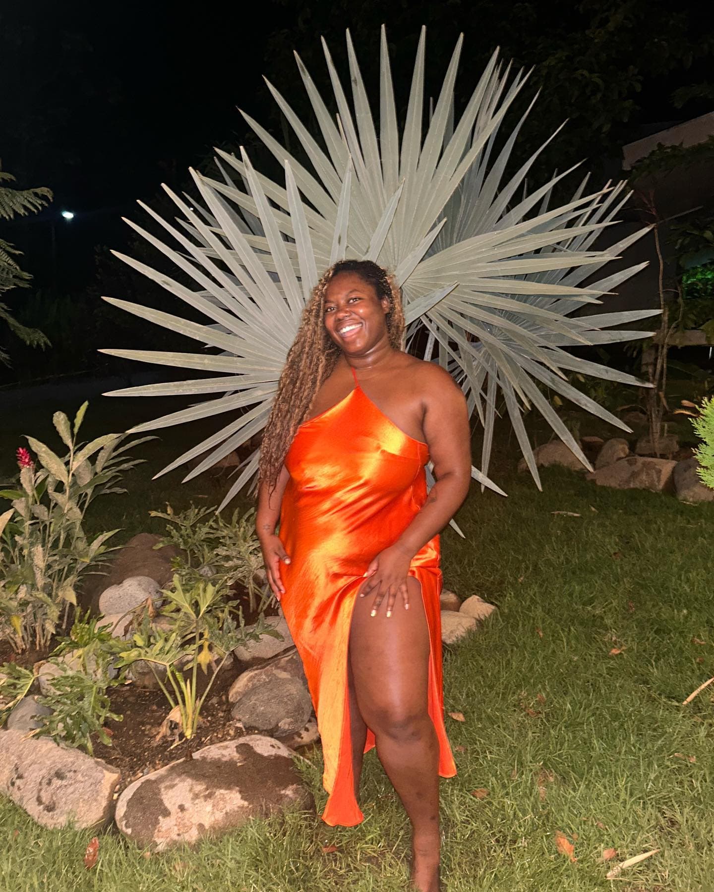 Advisor in a red and yellow evening dress posing outdoors at night in front of a tropical plant