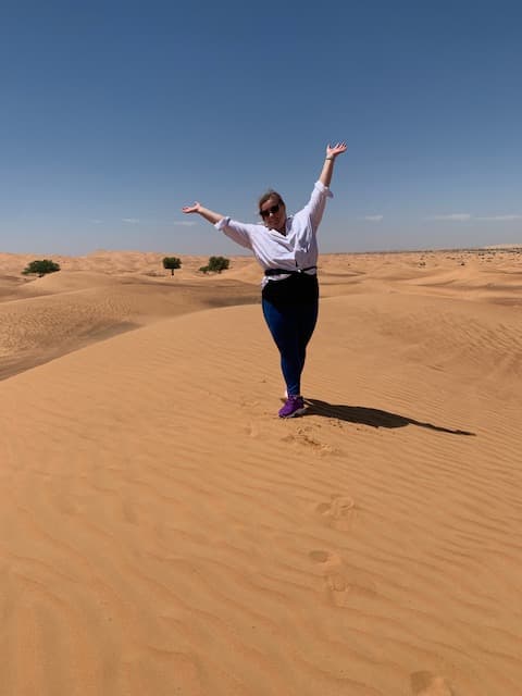 Advisor standing with arms raised to the sky in the middle of the desert