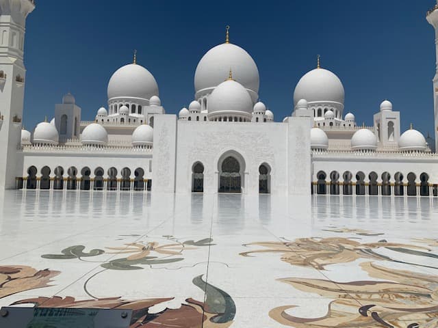 View of a large white mosque with marble floors under clear skies