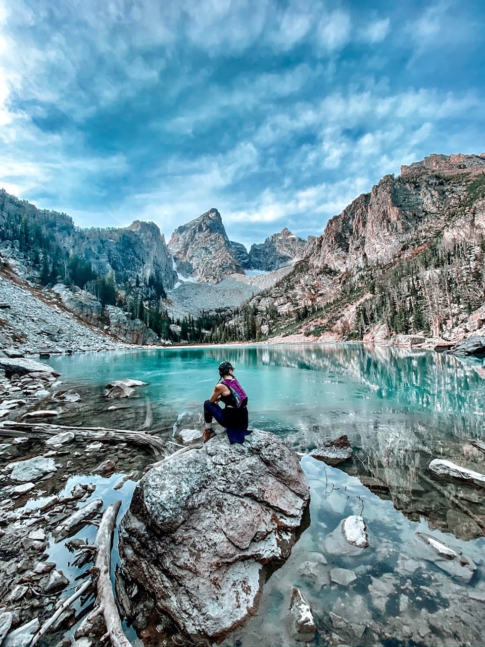 View of advisor sitting on a rock beside a glassy lake surrounded by stunning mountains