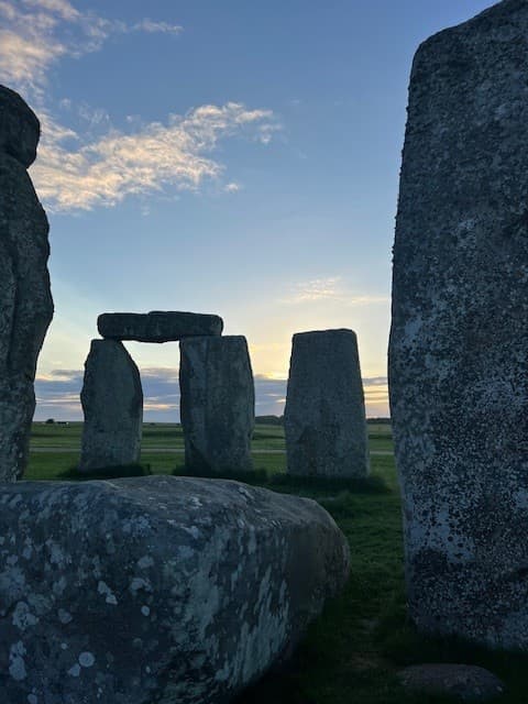 Stonehenge silhouetted against a vibrant sunset, with warm hues illuminating the ancient stones and surrounding landscape.