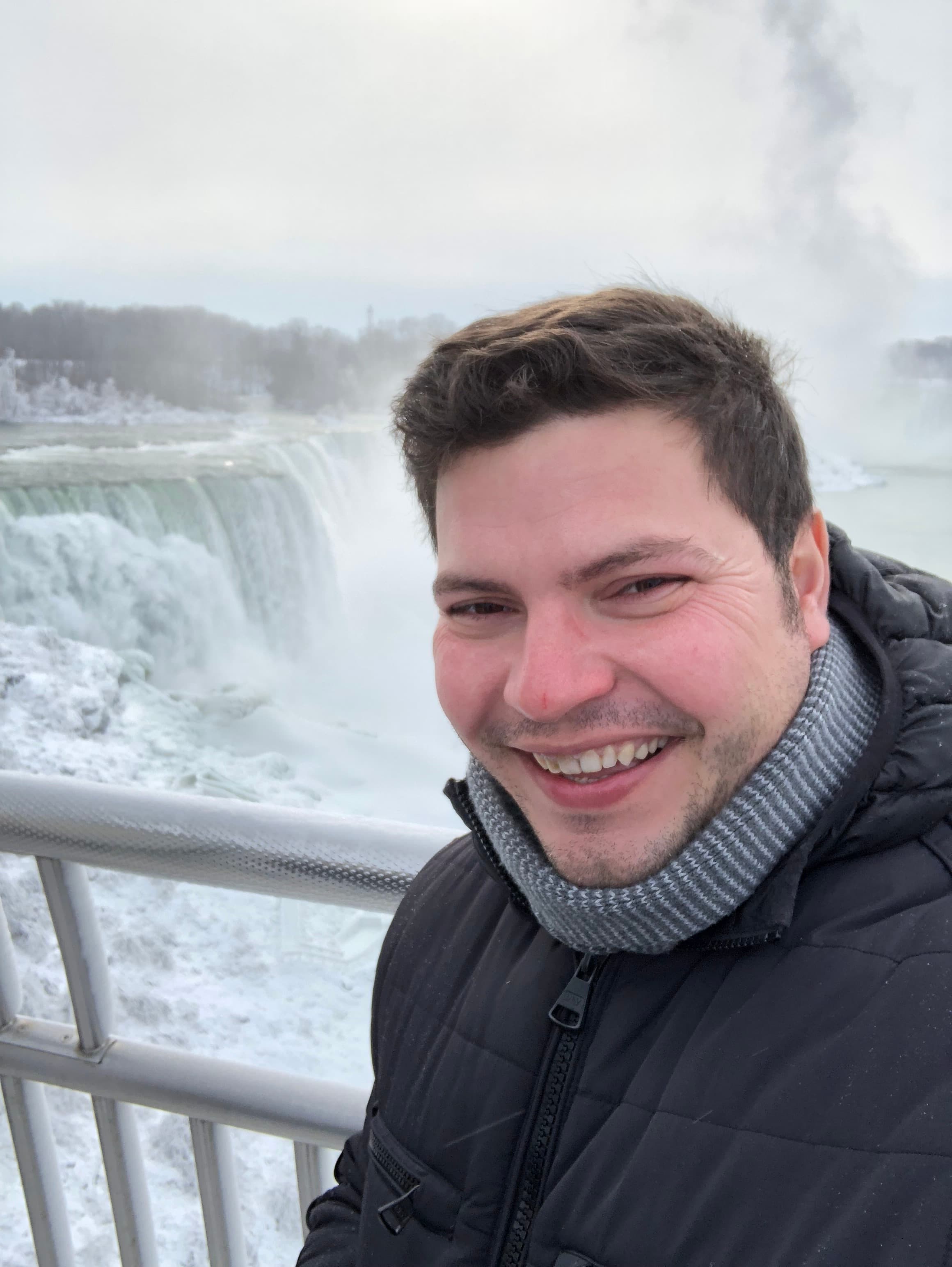 Advisor in winter clothing taking a selfie by a large waterfall on a cloudy day