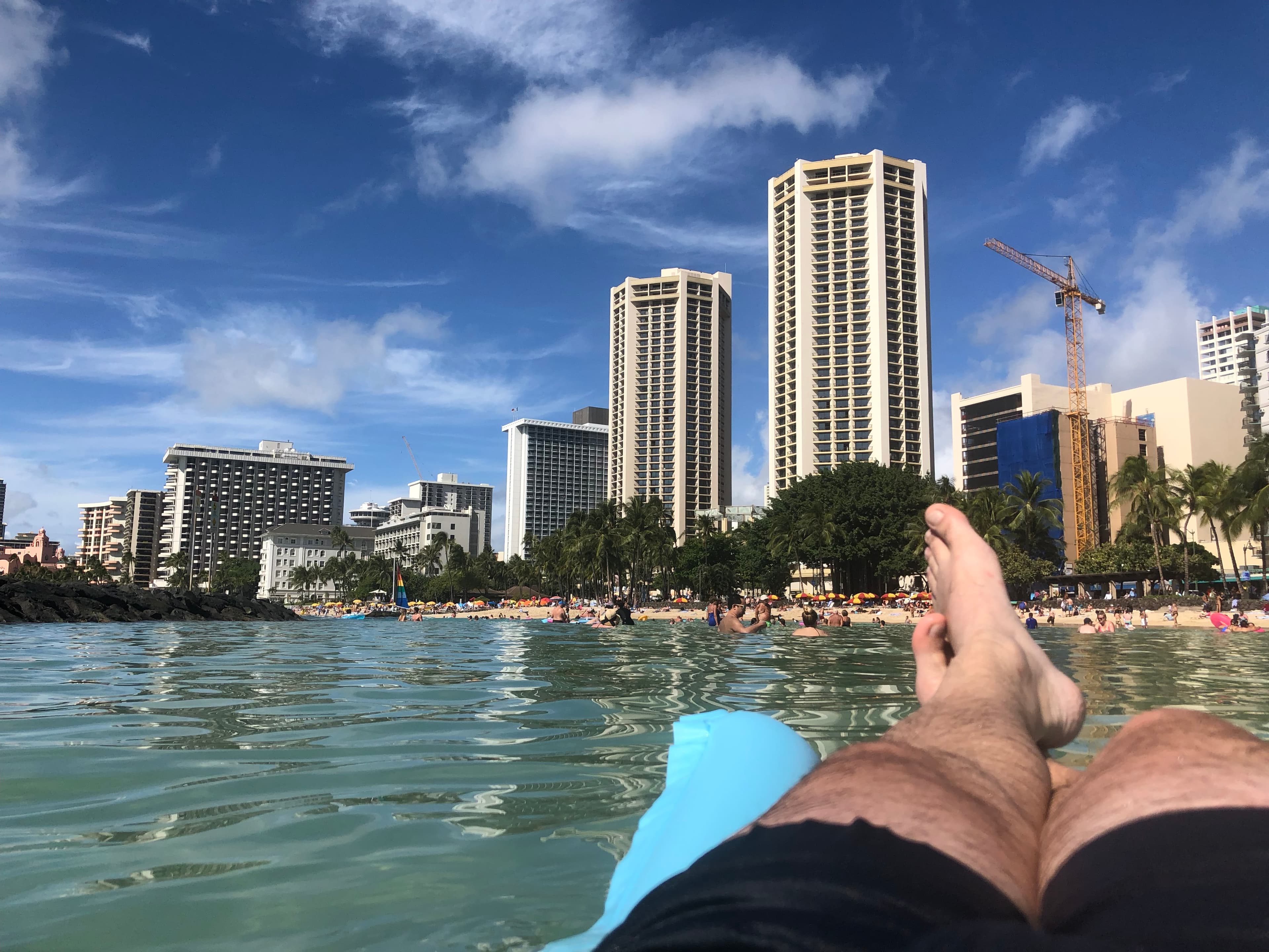 View of advisor’s legs on a raft with a city beach and tall buildings visible in the background