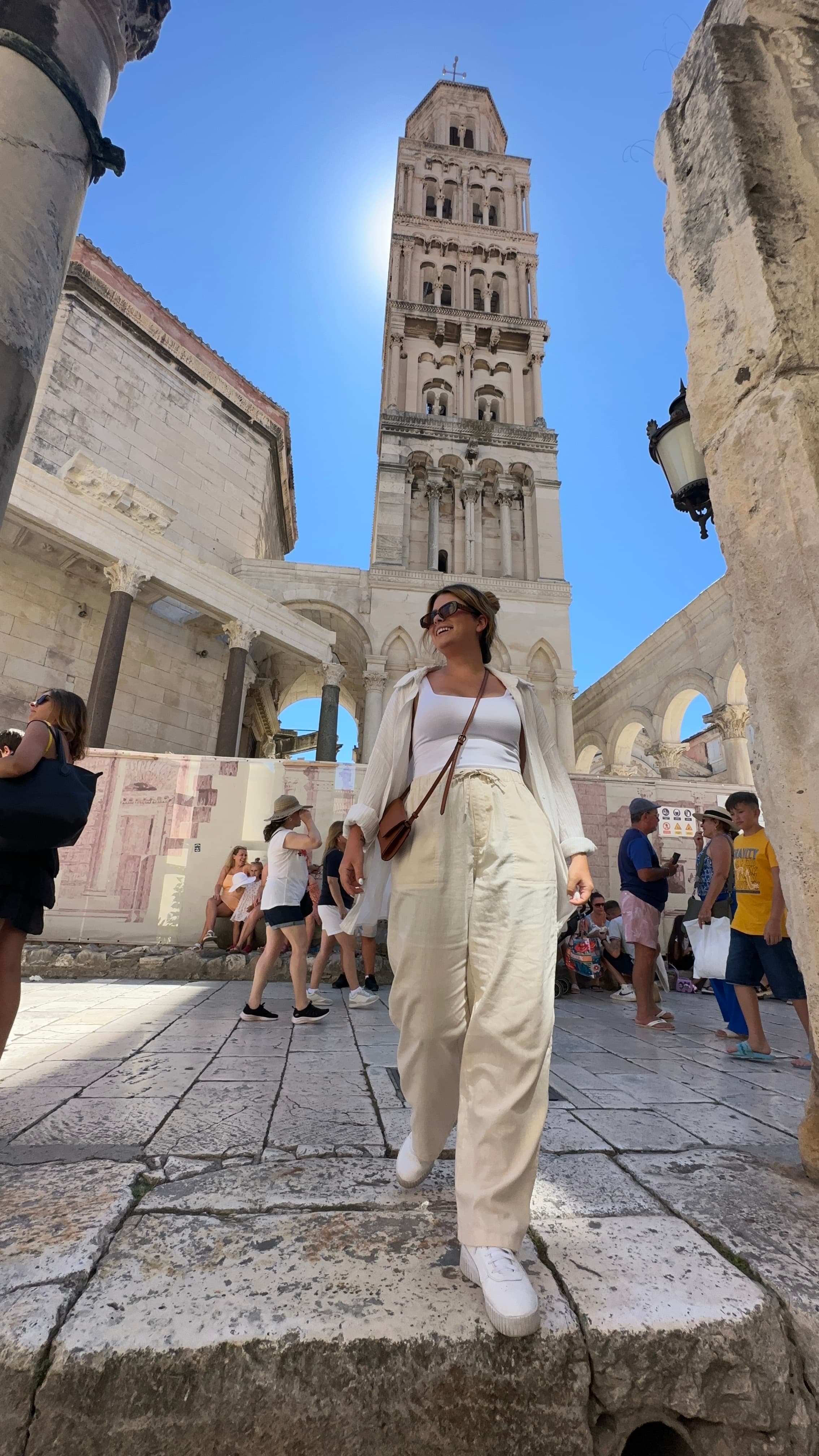 Advisor in an all-white outfit walking through an old city plaza with a tower visible behind her