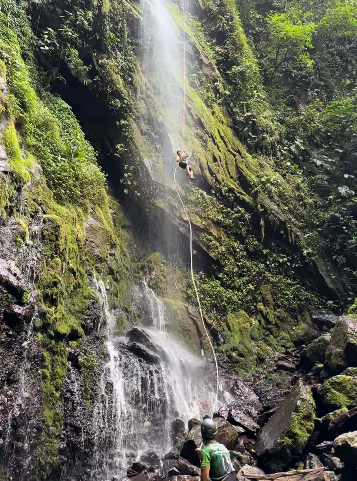 View of a waterfall in a lush jungle environment with tourists at the base