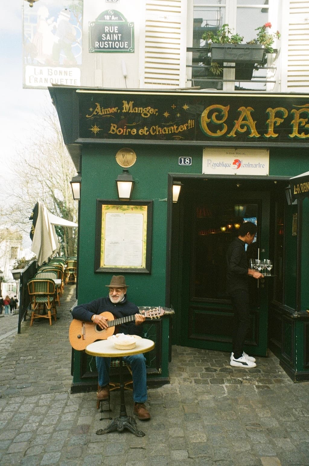 View of a man playing guitar outside the front of a green cafe