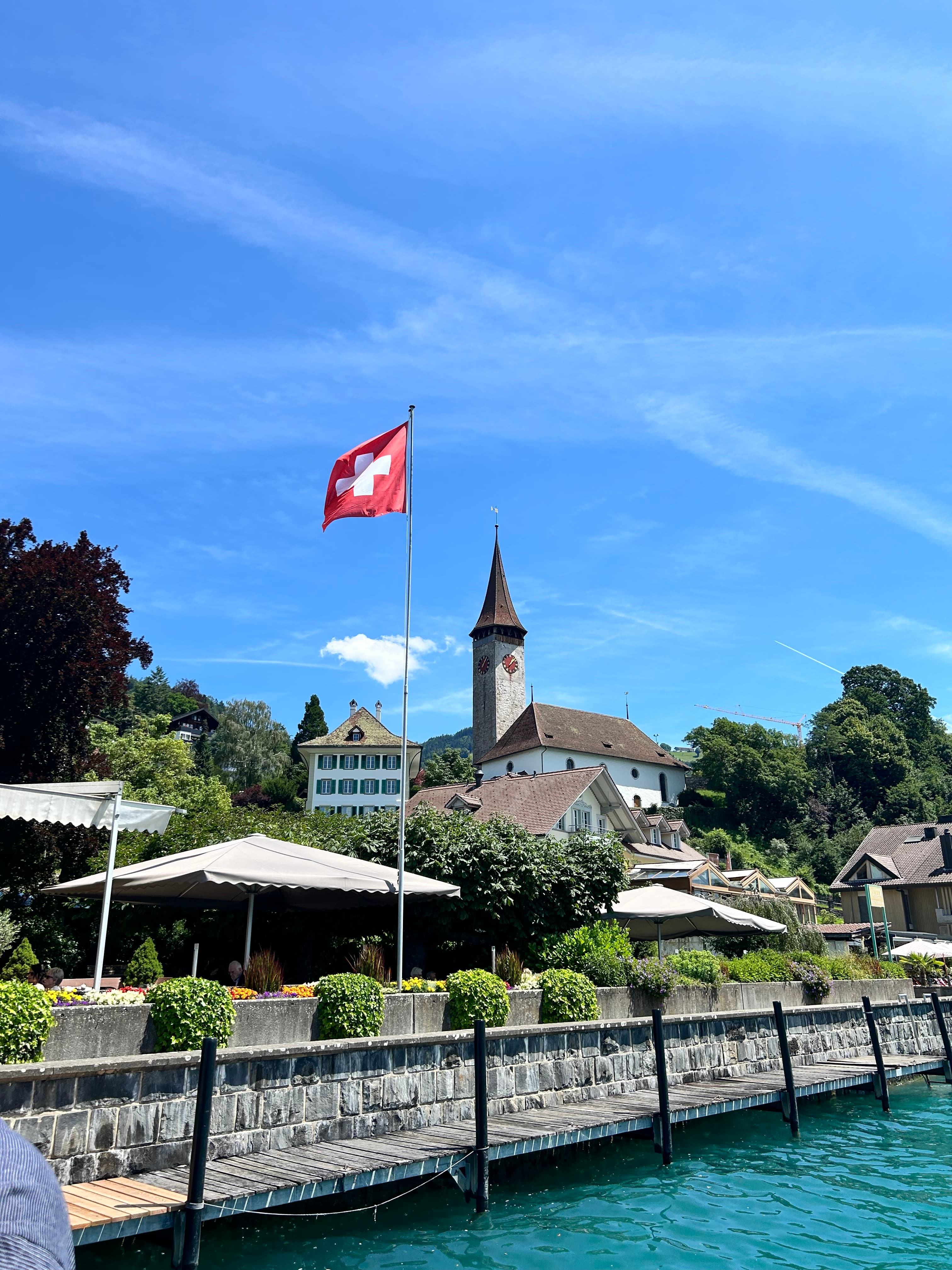 A view of water, a boardwalk, an old tower and a swiss flag. 