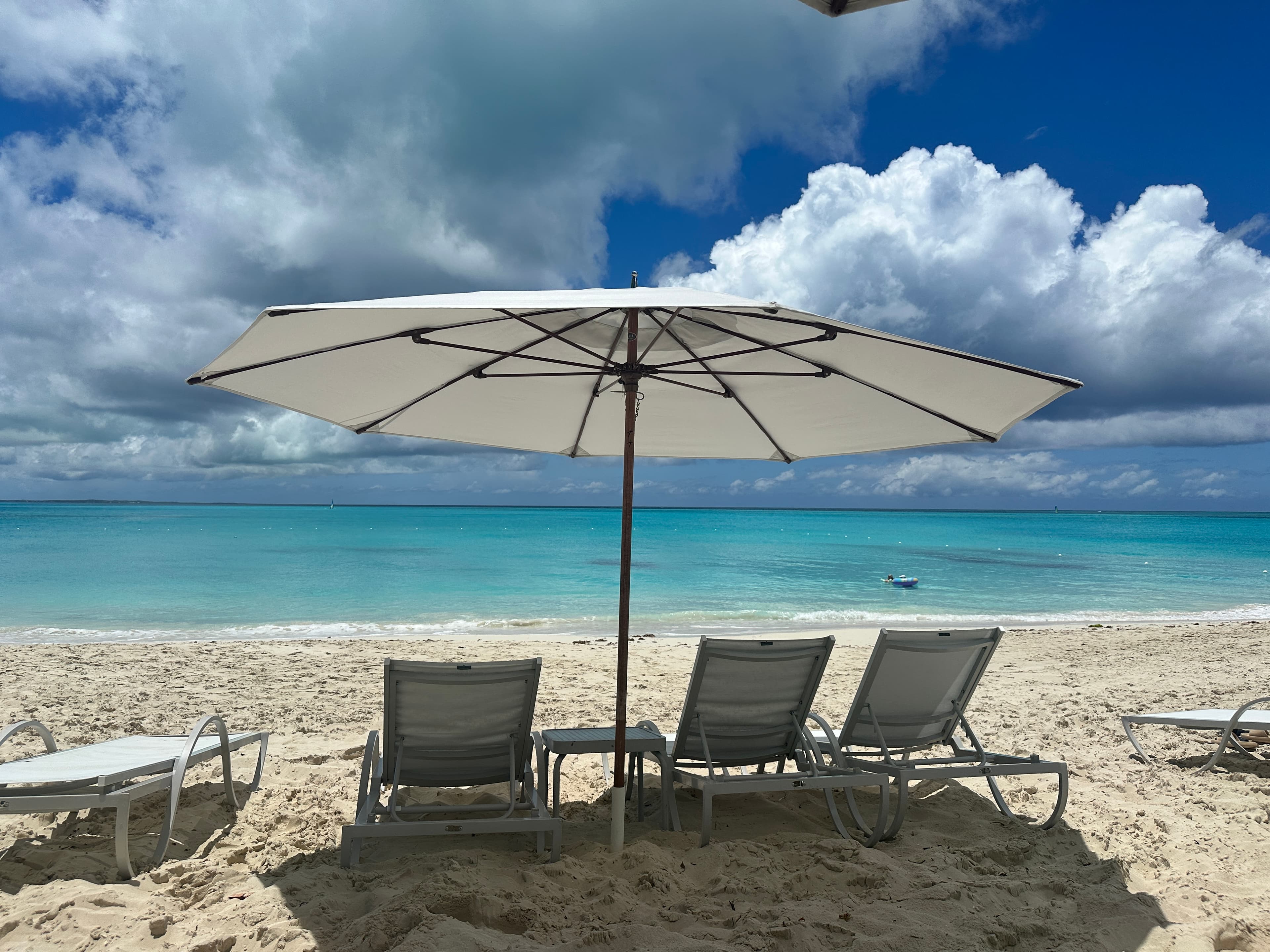 A white umbrella and lounge chairs on a beach facing the ocean.