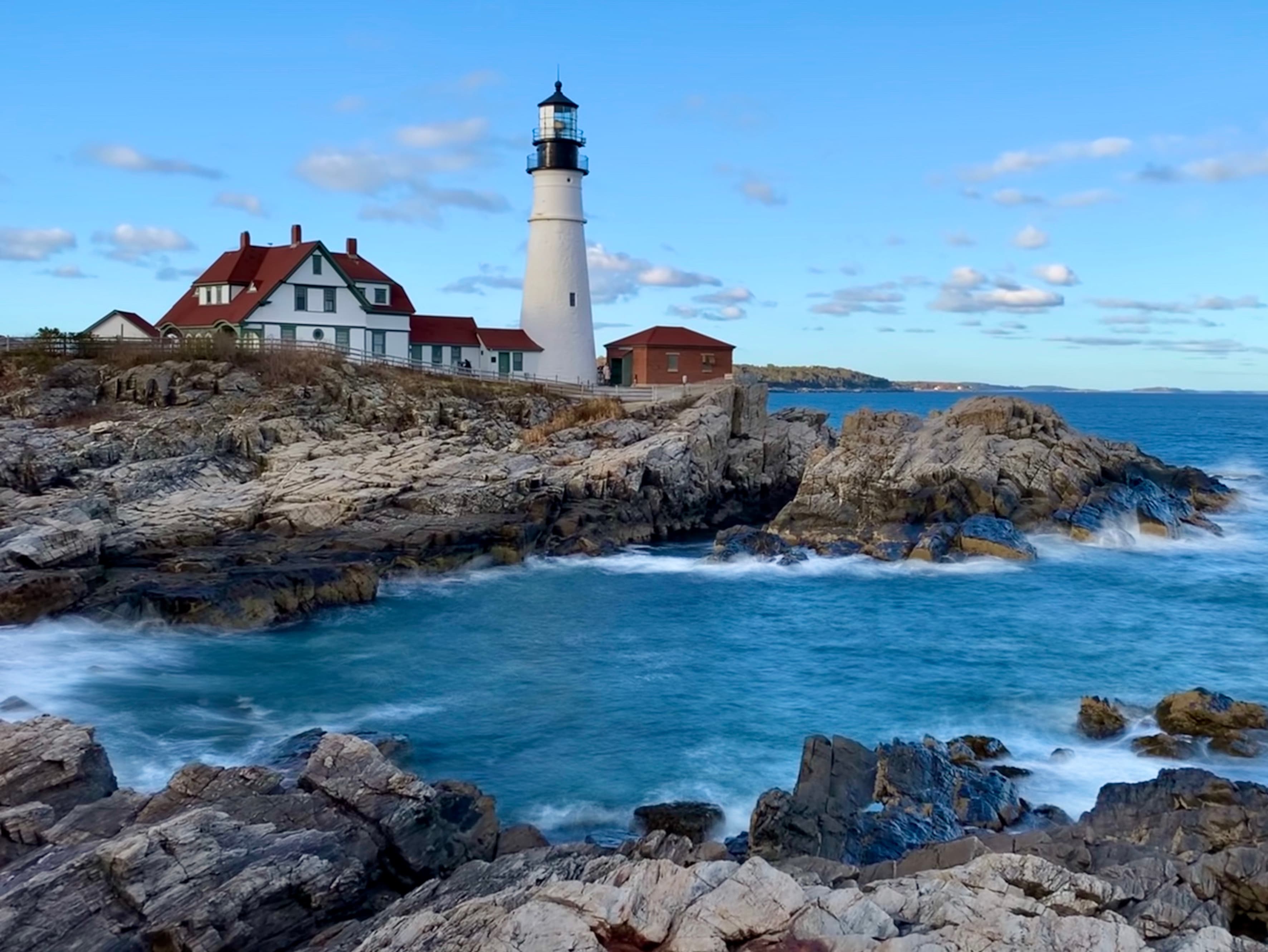 View of a white lighthouse on rocky cliffs on a sunny afternoon