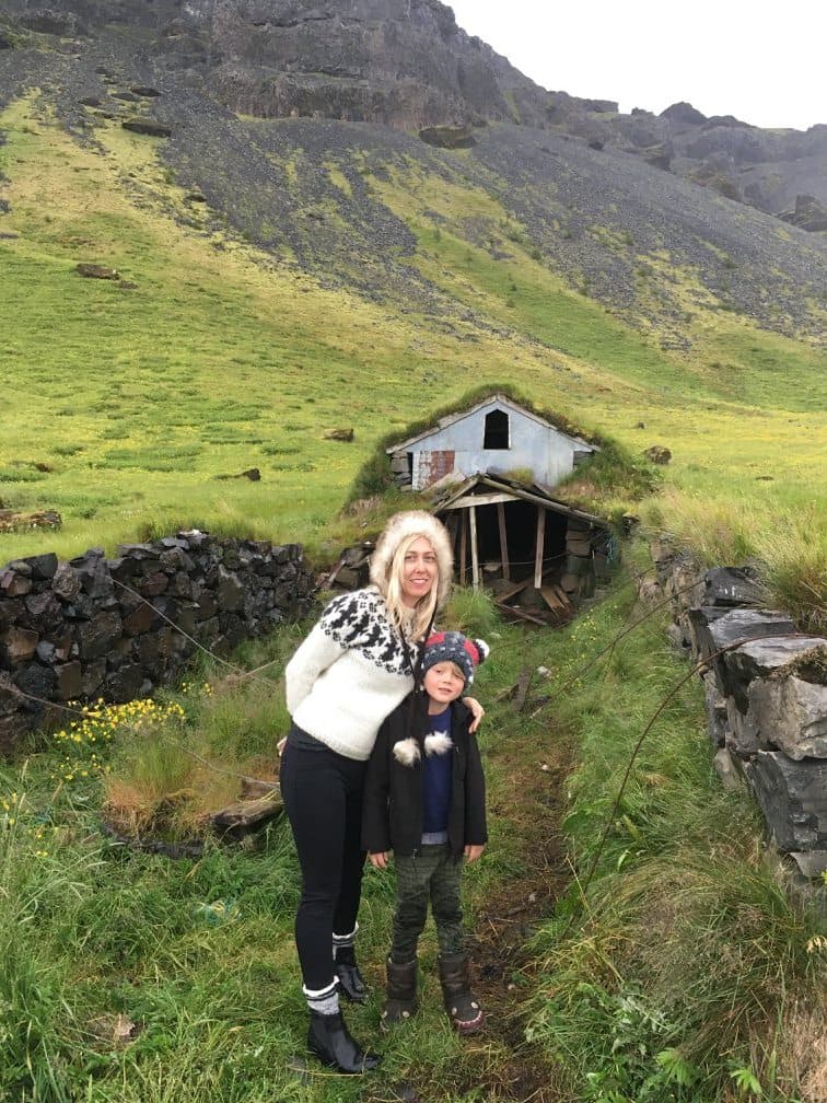 Advisor posing with a child in front of a small hut on a green mountainside in Iceland.