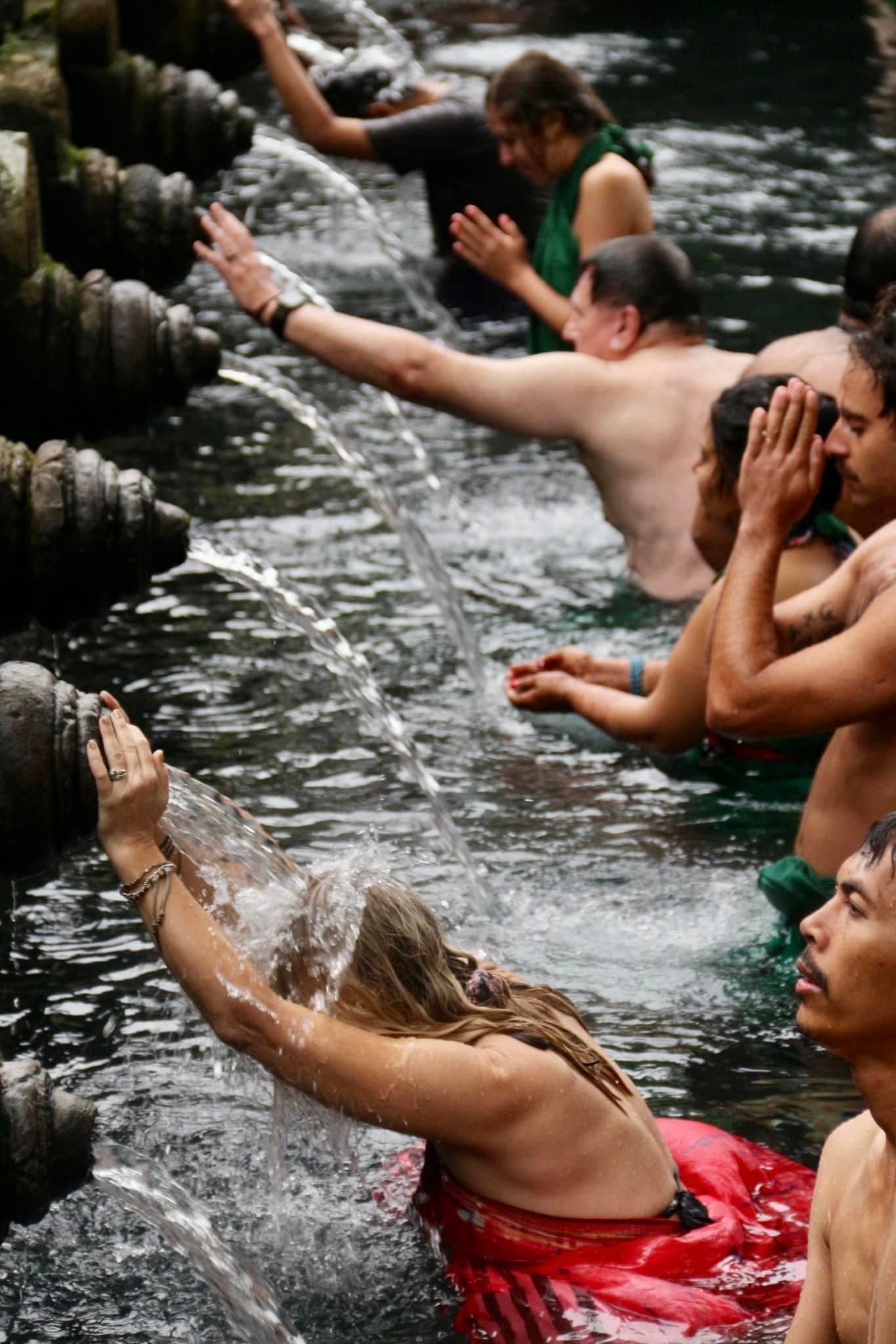 A row of people standing in water, each with a flowing fountain in front of them pouring on their hands and body.