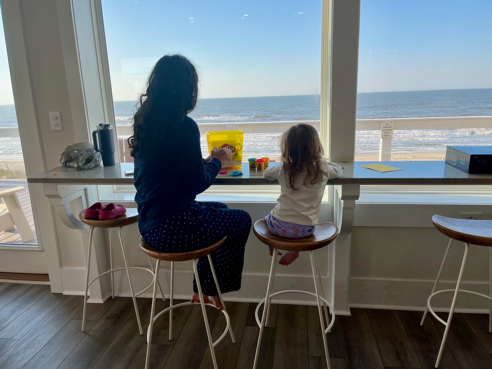 Two people sitting at a counter looking at the ocean through the window.