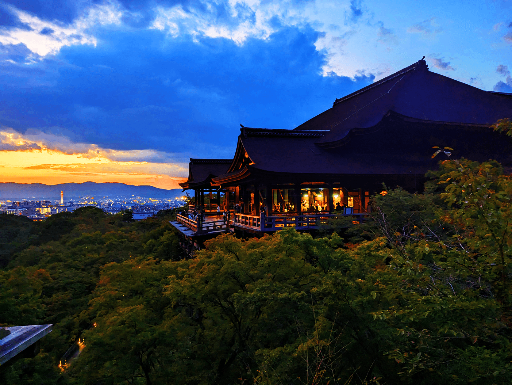 Sun sets in the distance overlooking a hilltop structure lit from within. 