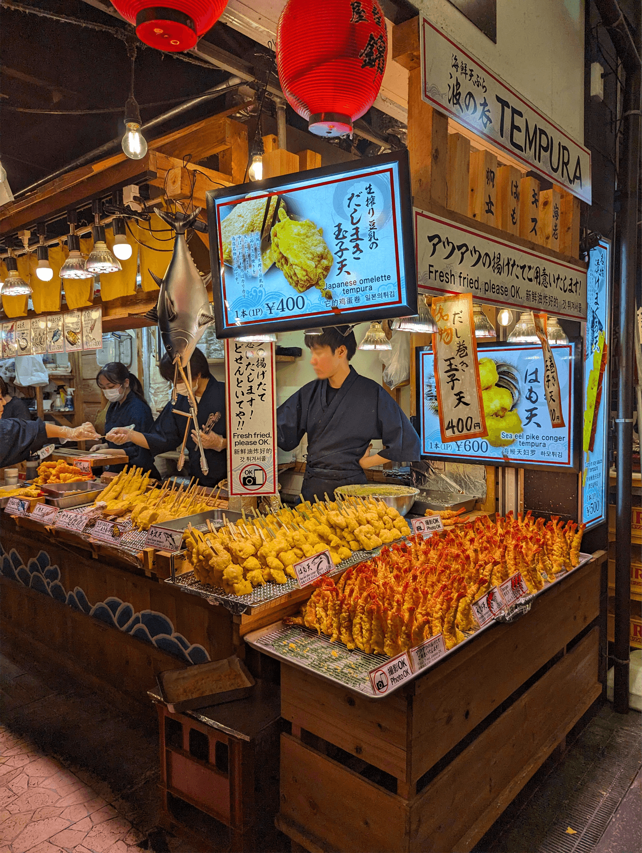 A open-air market with brightly-lit stalls shows its wares and seafood on ice. 