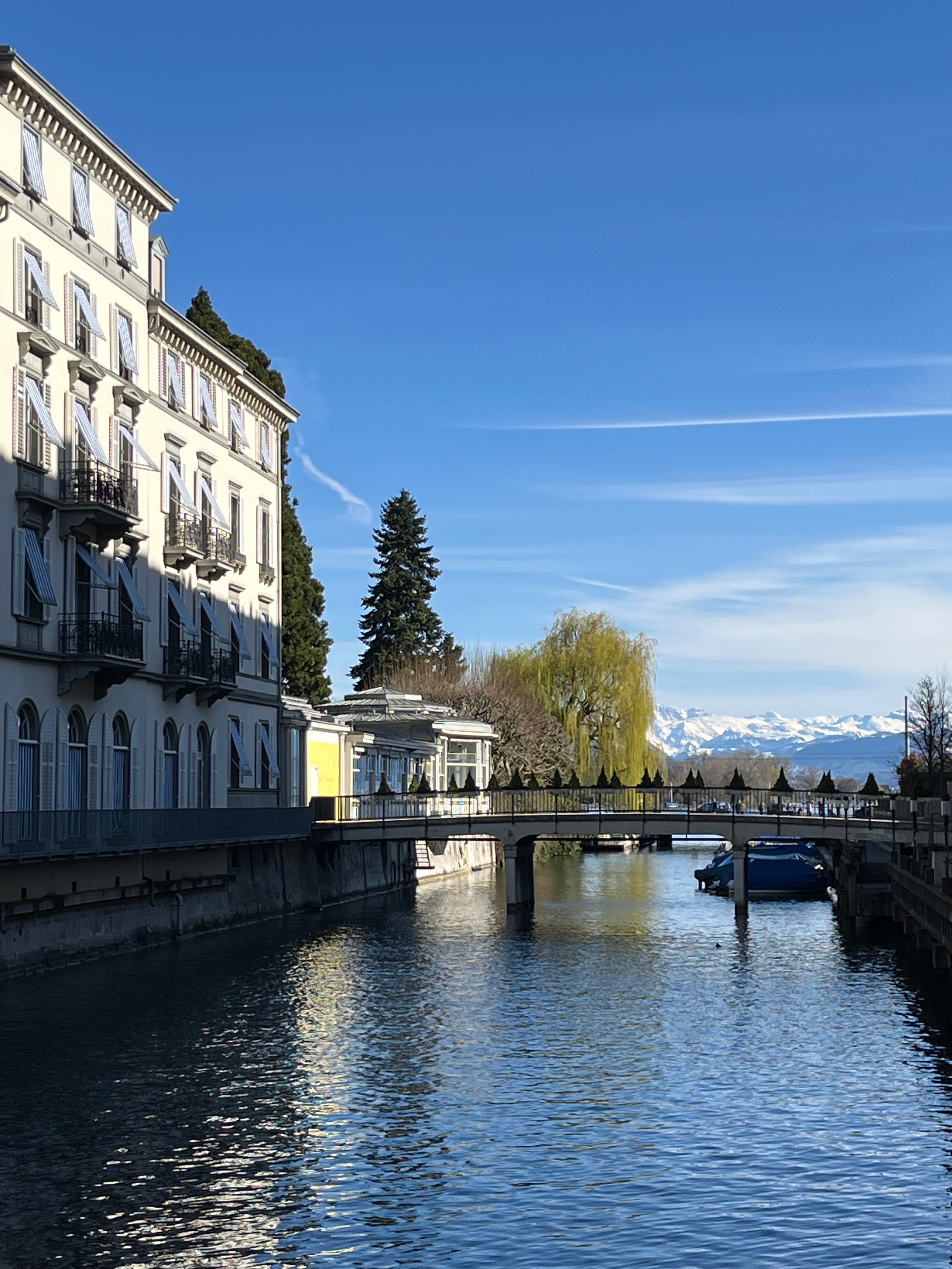 A river running down the middle of a city with a walking bridge over it.