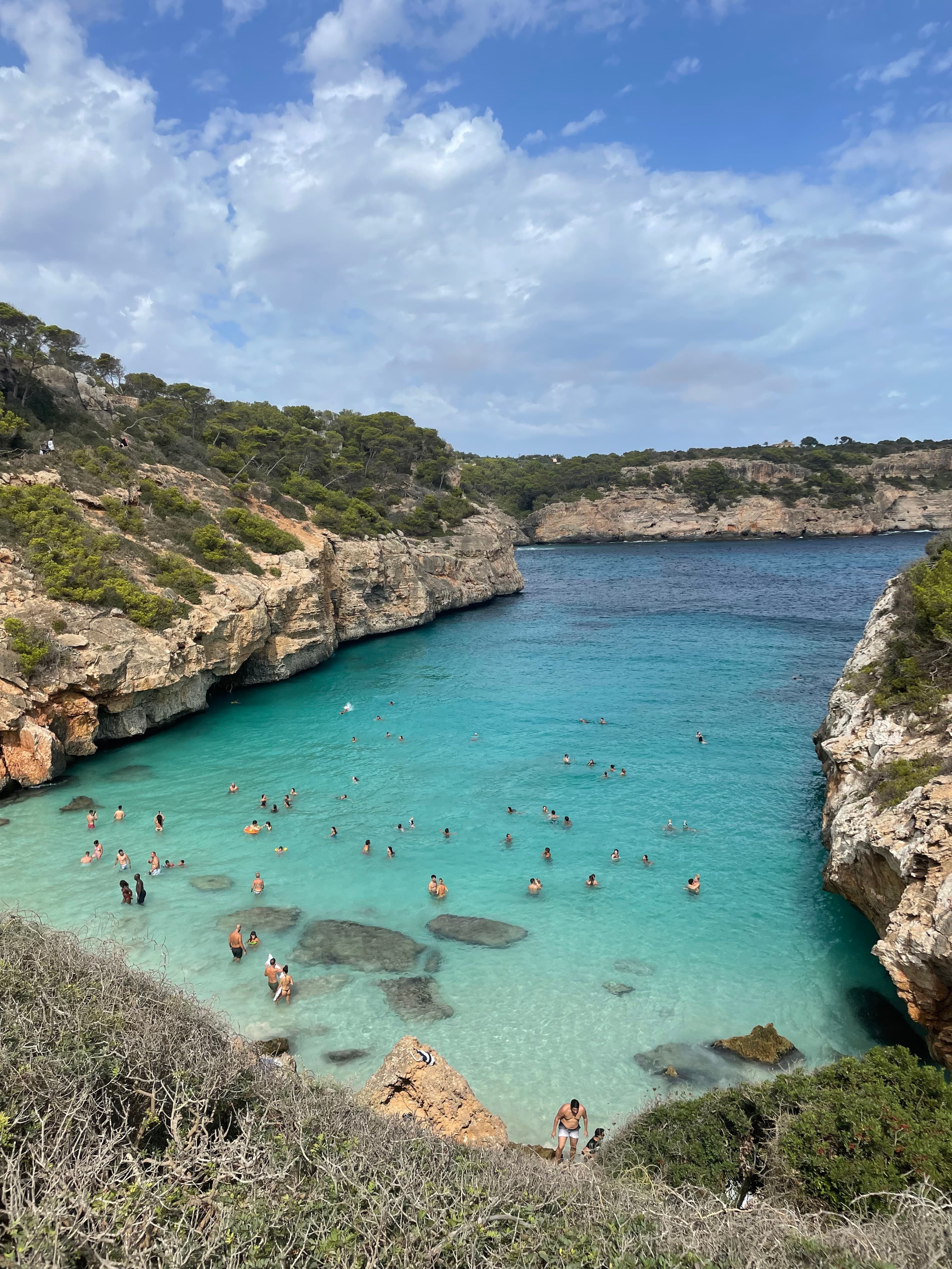 A beautiful view of a turquoise lagoon in Mallorca with people swimming in the water. 