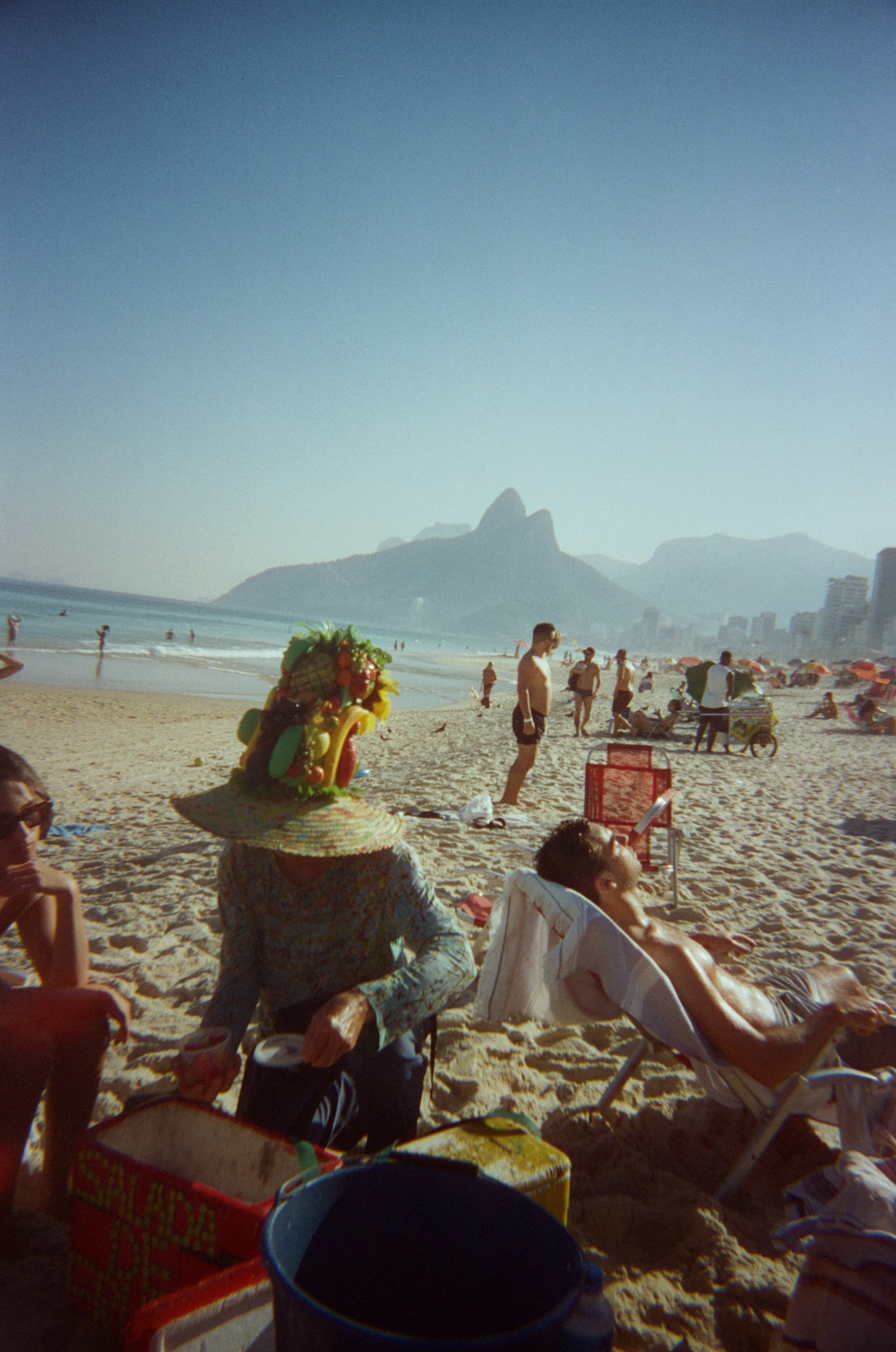 View of people sunbathing on a wide beach under clear skies with a mountain in the distance