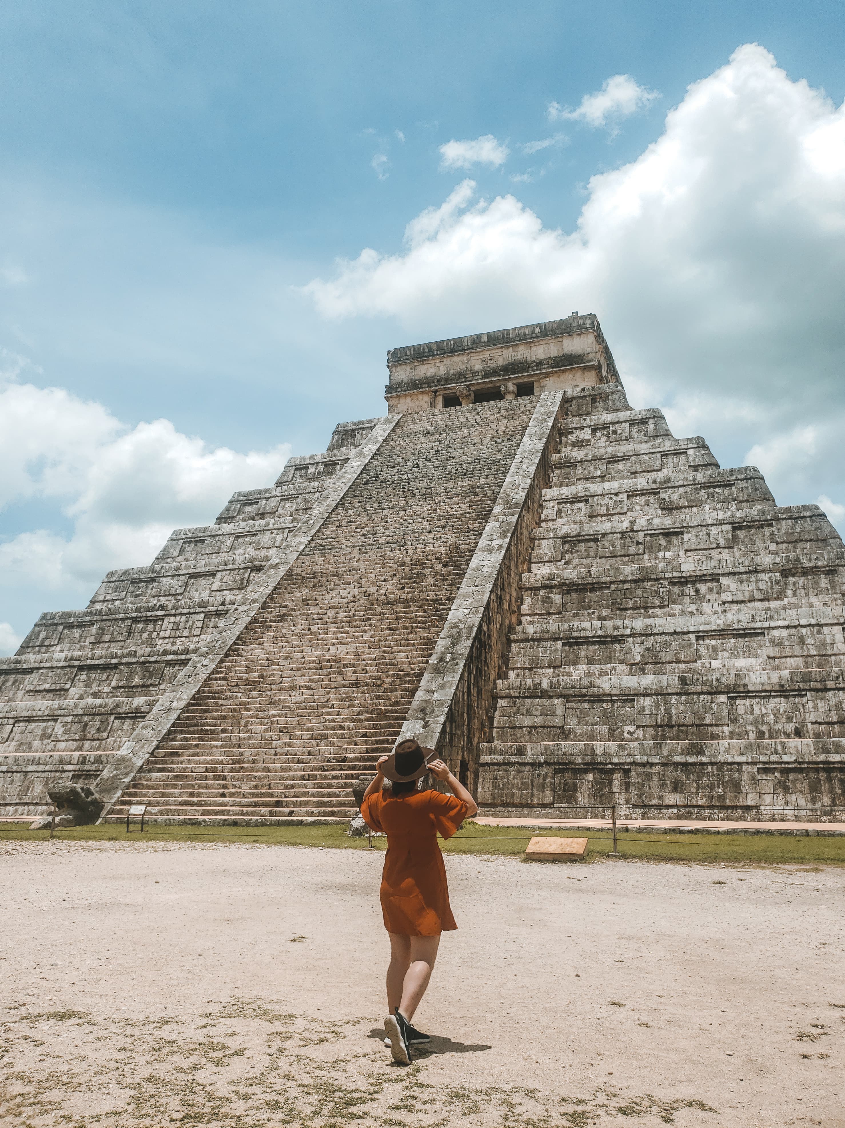 A woman posing in front of a pyramid in Mexico. She is wearing a red dress. 