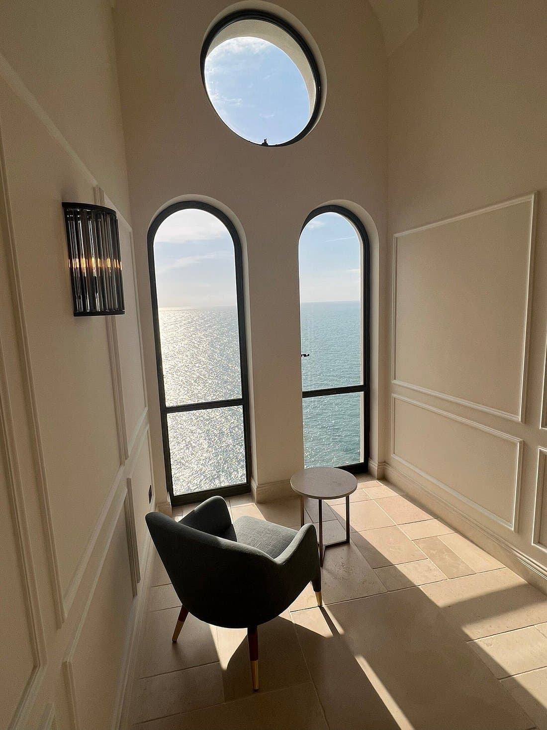 View of a chair and small round table in front of two windows overlooking the sea