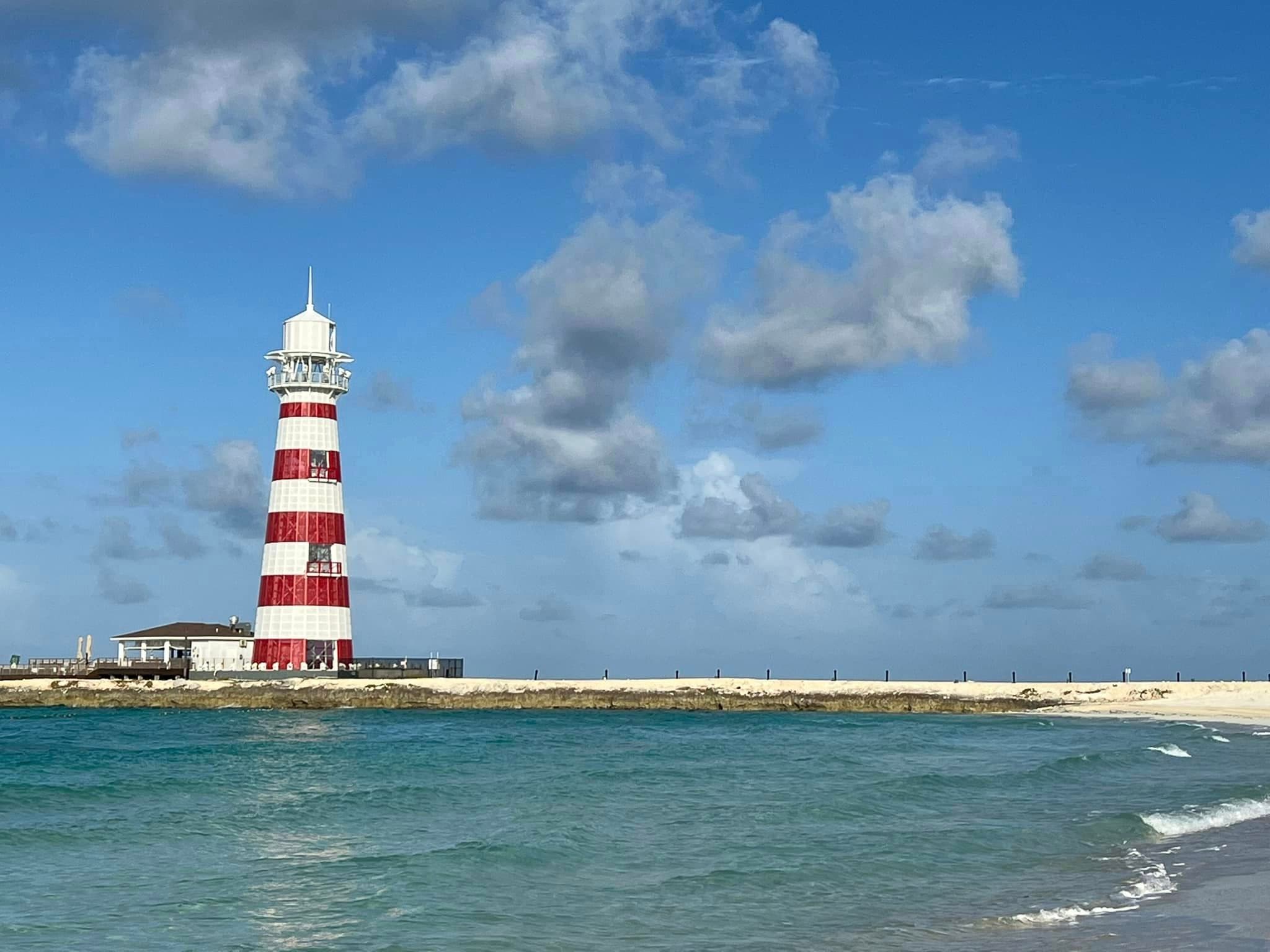 View of a red and white striped lighthouse on a sandy beach on a sunny day