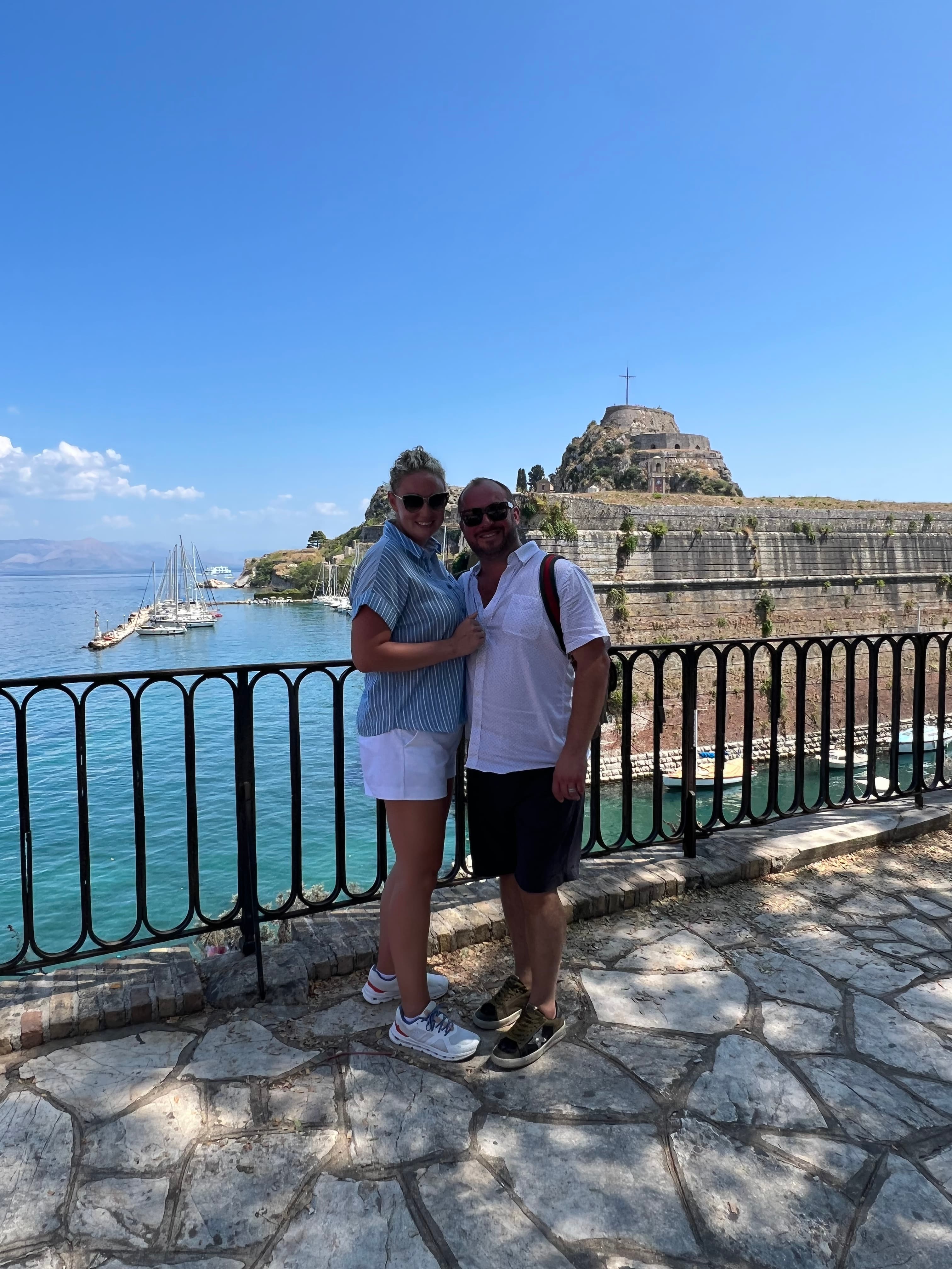 Advisor and partner smiling side by side at a viewpoint overlooking the sea under clear skies