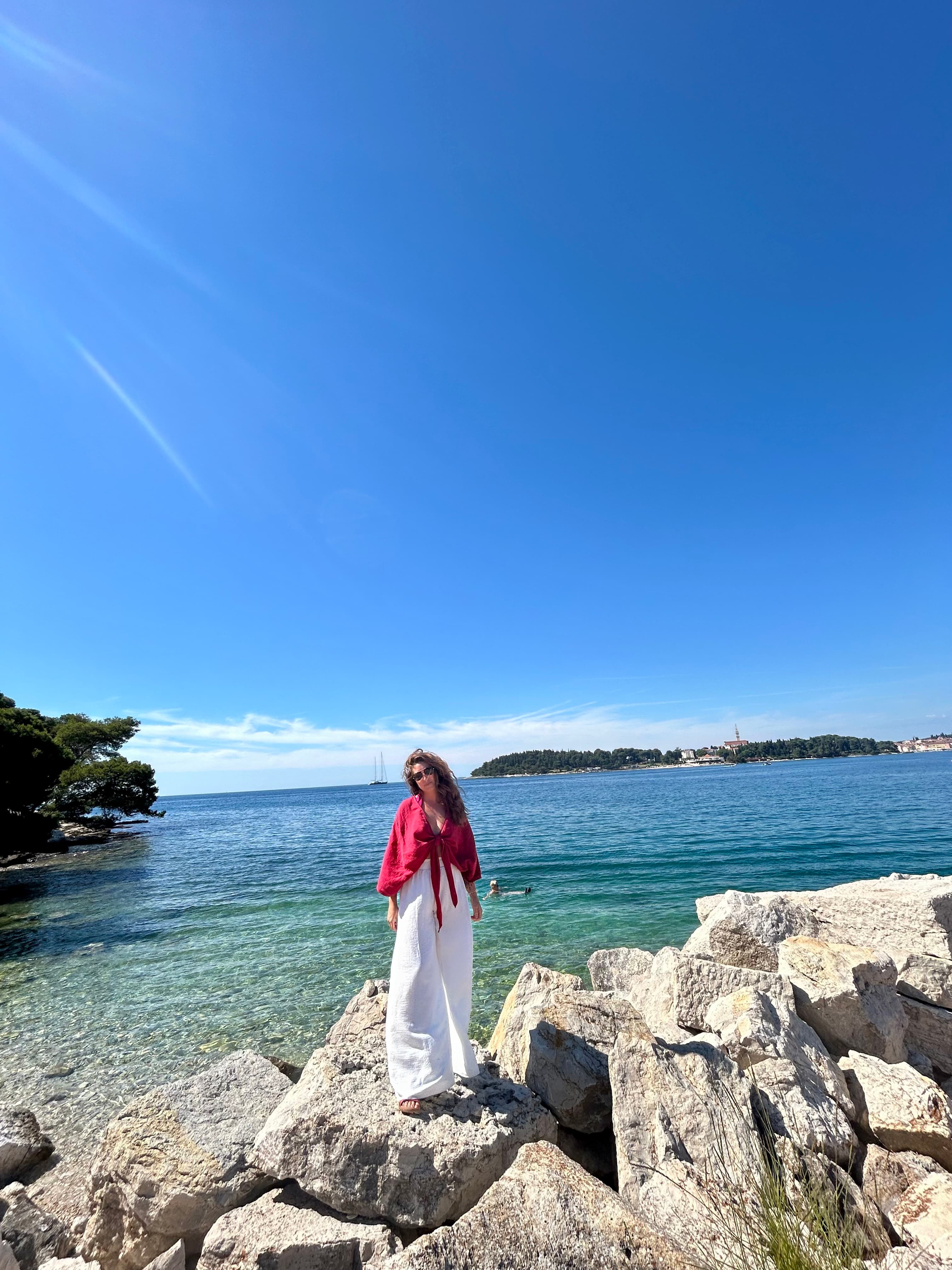 A woman standing on rocks next to a body of water shore line