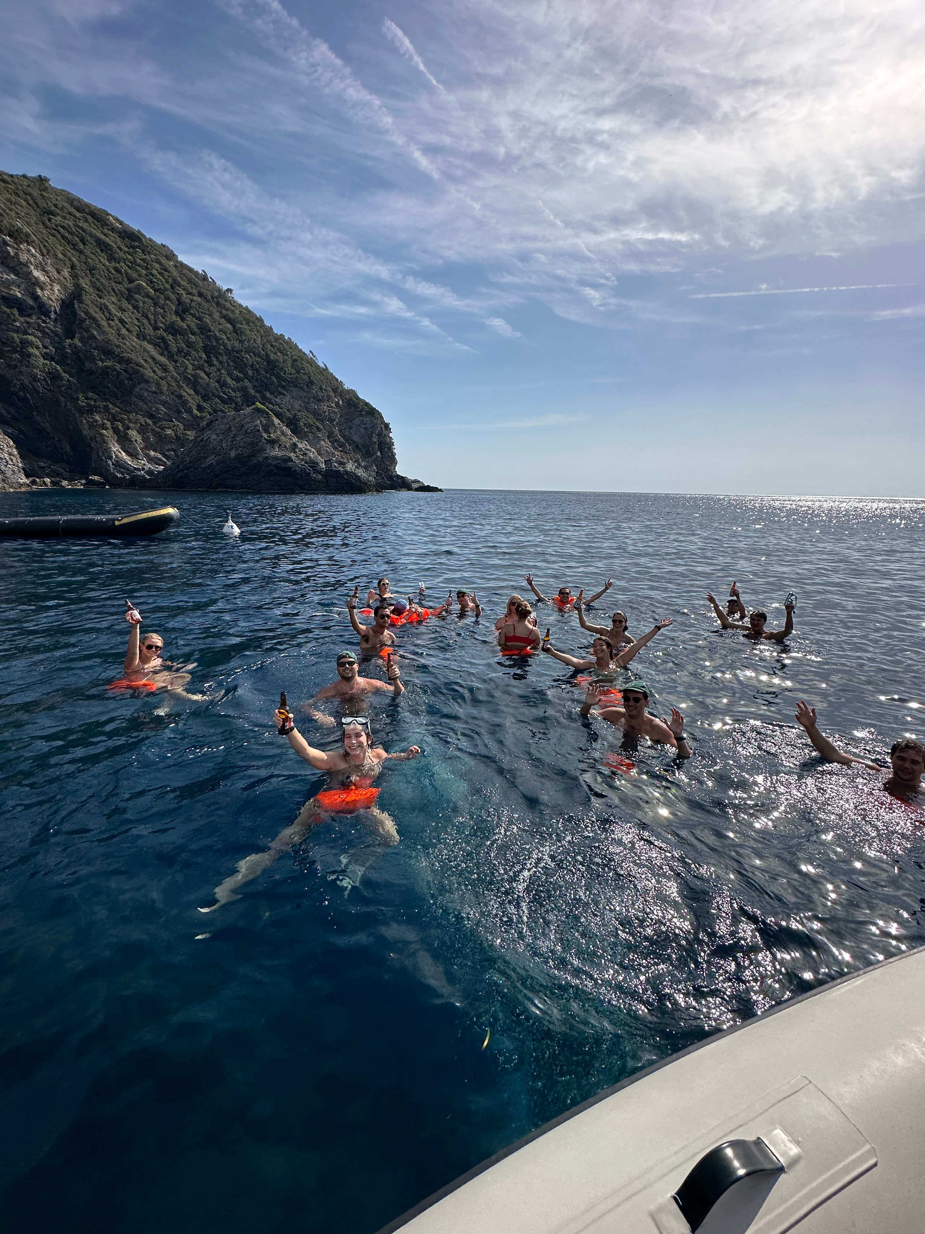 View of a group of people swimming in the ocean off the side of a boat on a sunny day