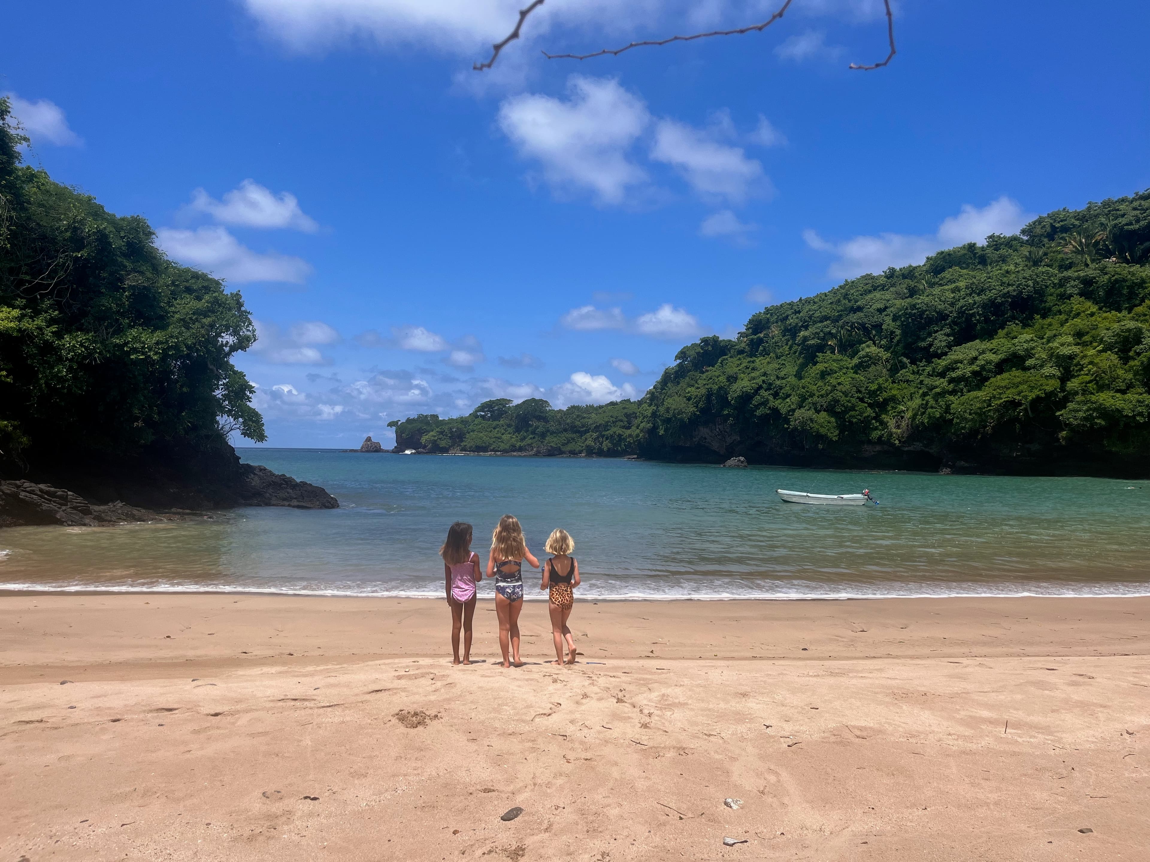 View of three woman standing on an empty beach and looking out towards the calm water