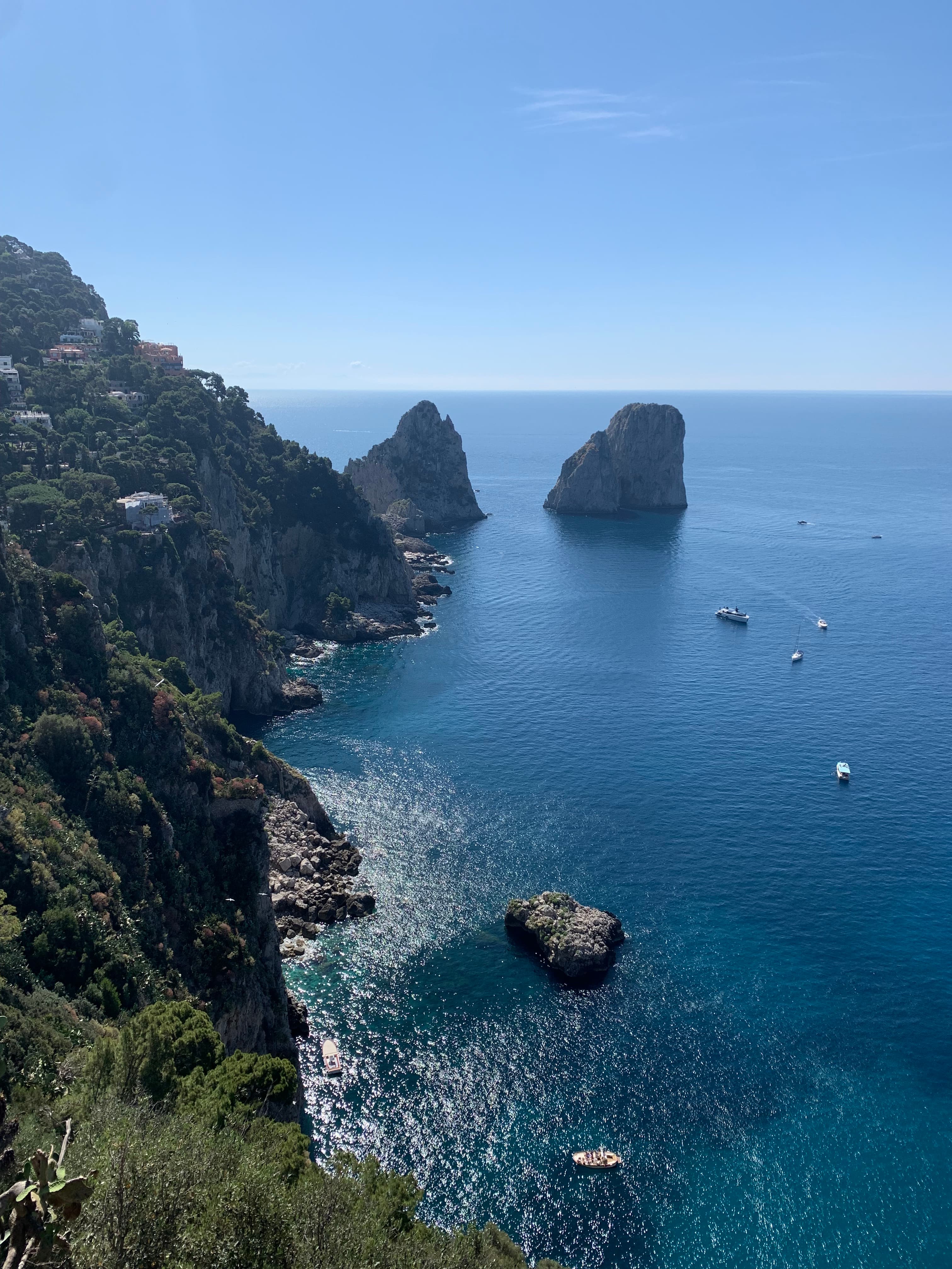 A coastal view of a crag-filled hillside as waves lap the shore on a sunny day. 