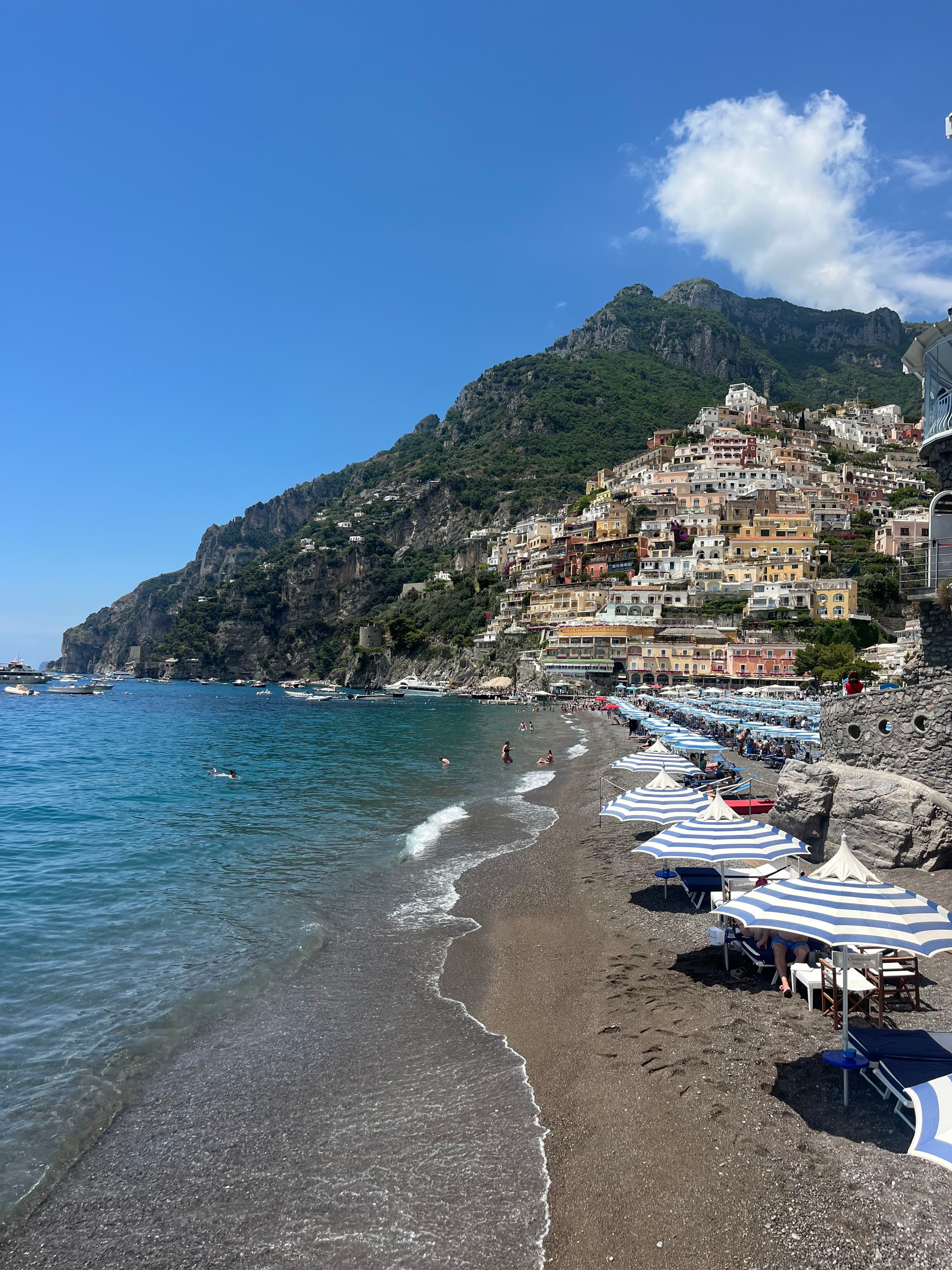 A hillside town built against the rocks overlooks crystal-clear waters as waves lap the shore on a sunny day. 