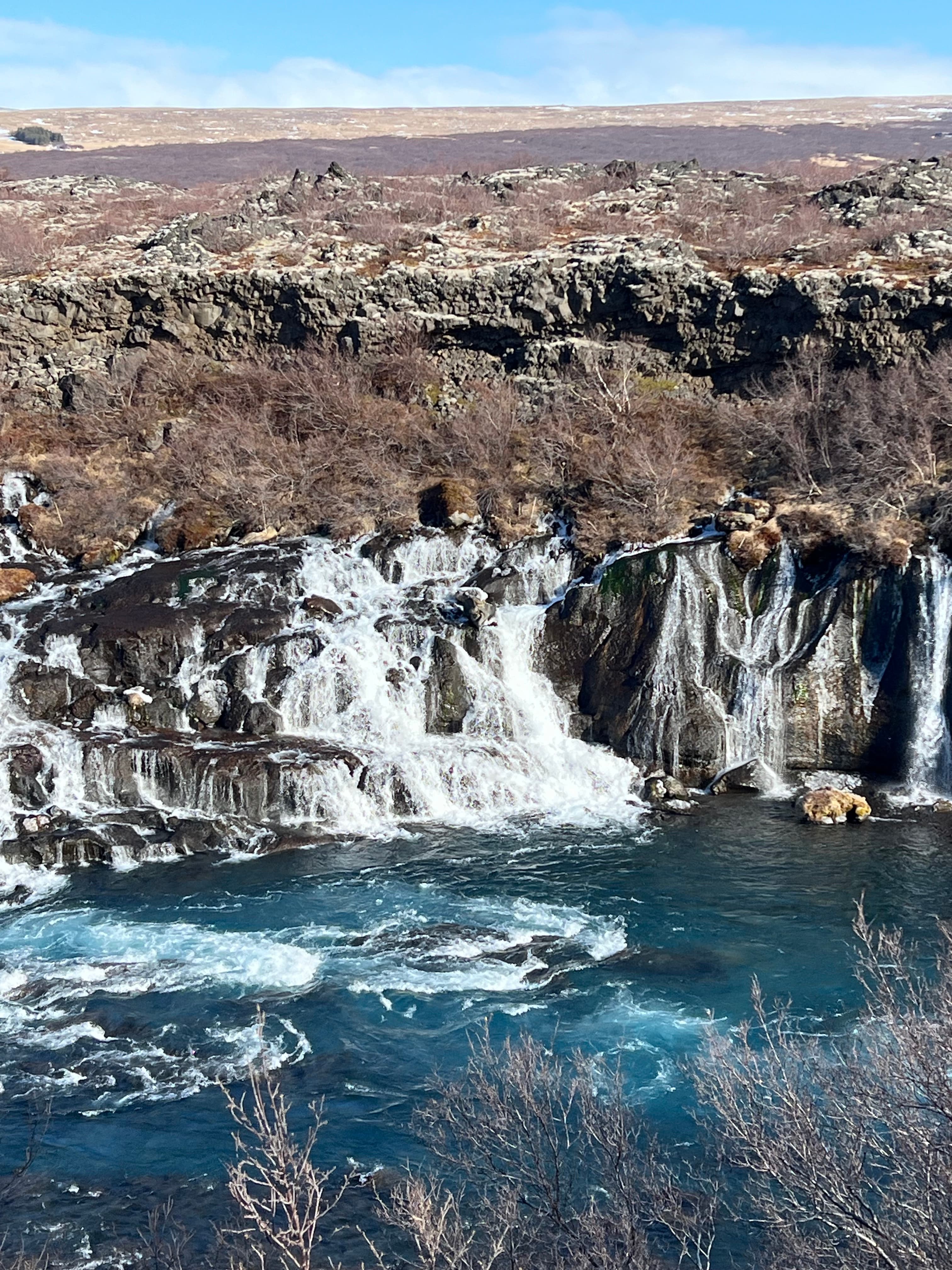 Aerial view of stunning waterfalls pouring into a deep blue body of water under sunny skies