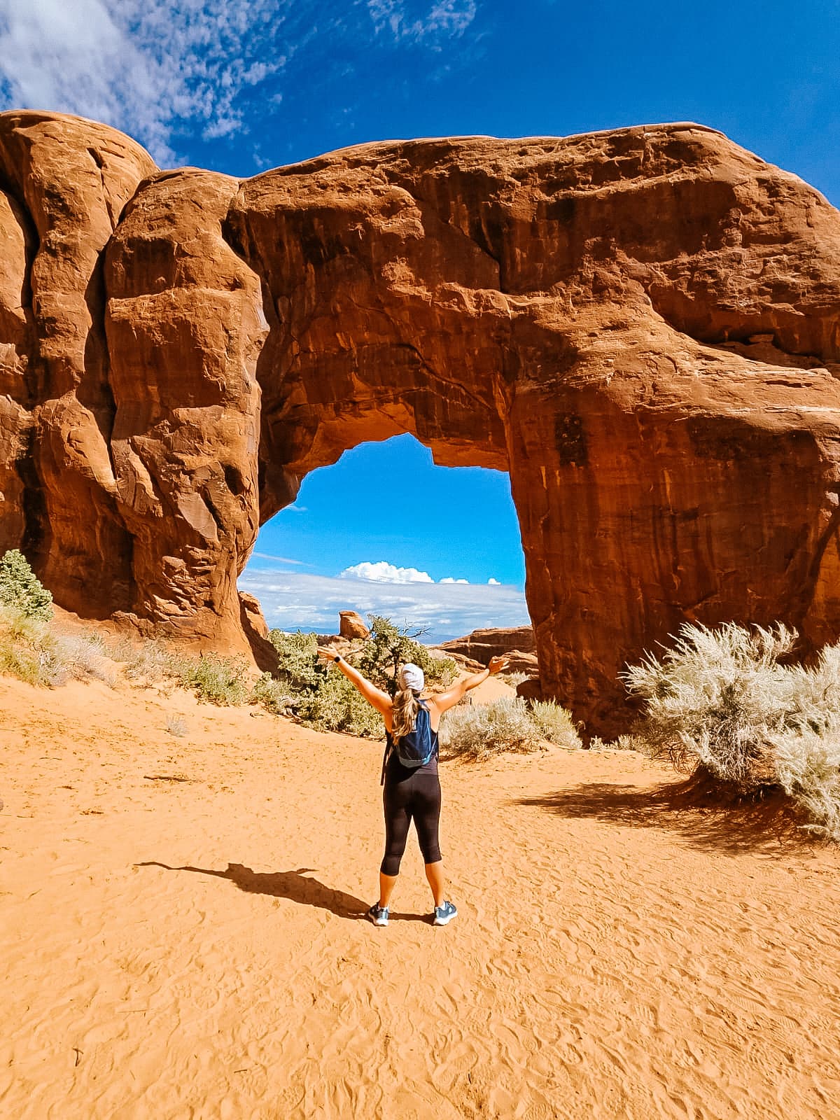 Advisor posing with arms raised in front of a red rock formation with an arch in the center