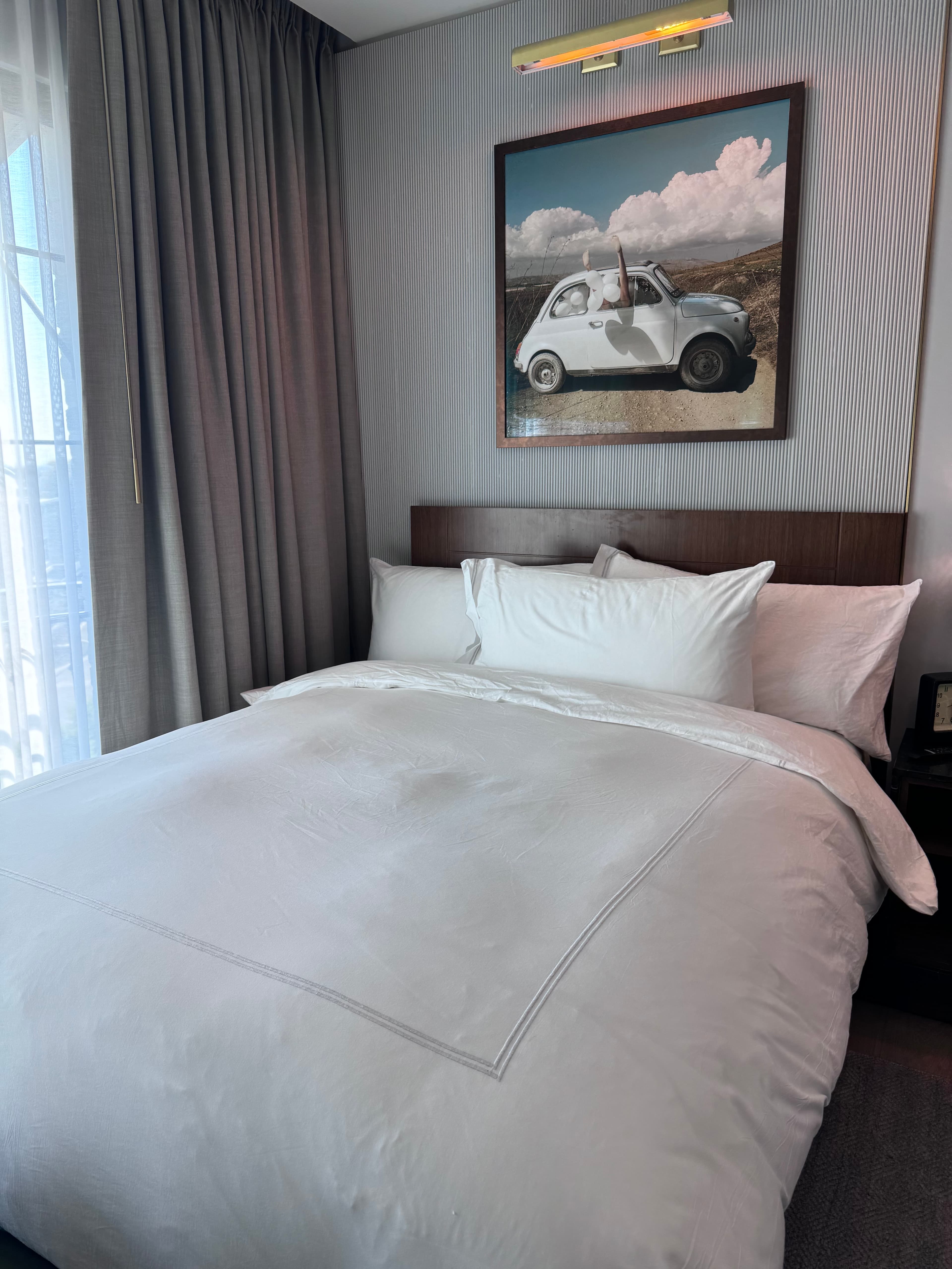 View of a neatly made hotel bed with white bedding and an image of a car on the wall above
