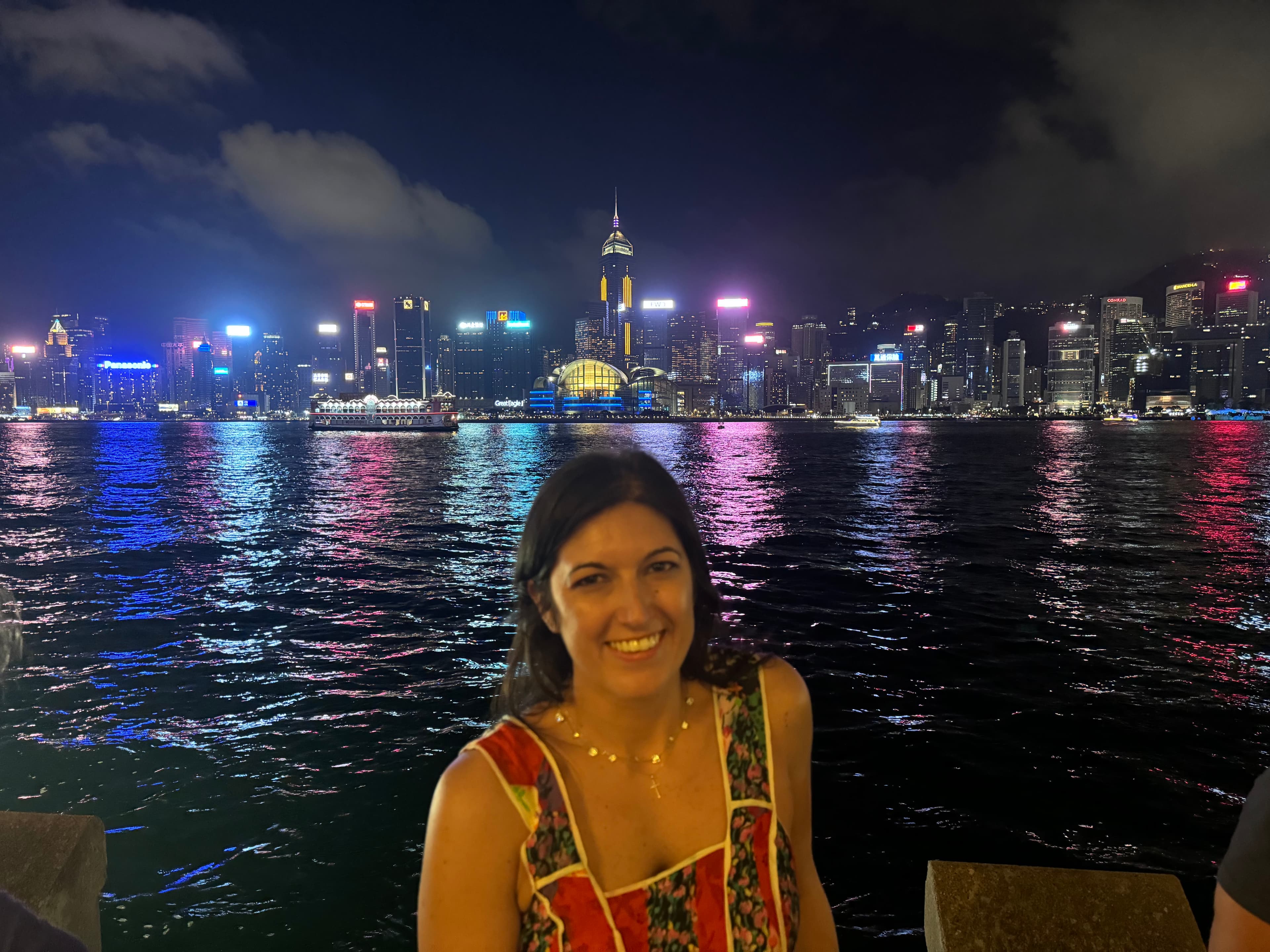 Advisor smiling on the waterfront with a brightly lit cityscape on the horizon